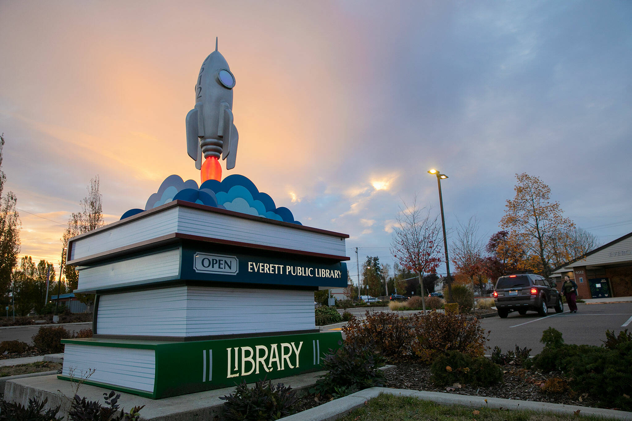 The sun sets beyond the the Evergreen Branch of the Everett Public Library as a person returns some books on Nov. 11, in Everett. (Ryan Berry / The Herald)