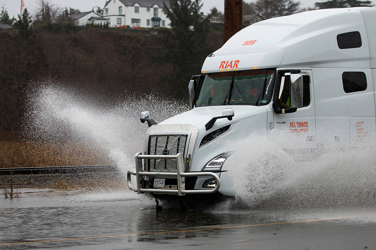 A semi truck sprays water as it drives along a flooded Marine View Drive on Tuesday, Dec. 27, 2022 in Everett, Washington. (Olivia Vanni / The Herald)