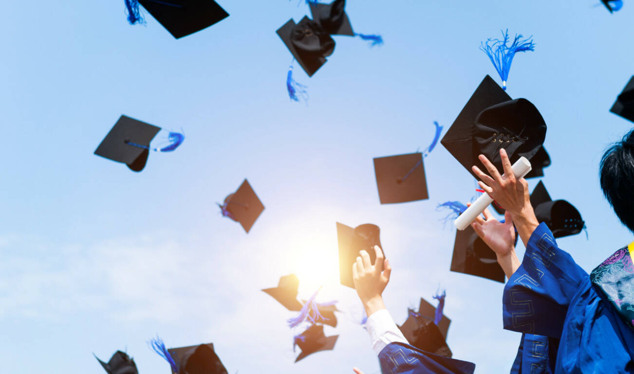 Graduating students hands throwing graduation caps in the air.