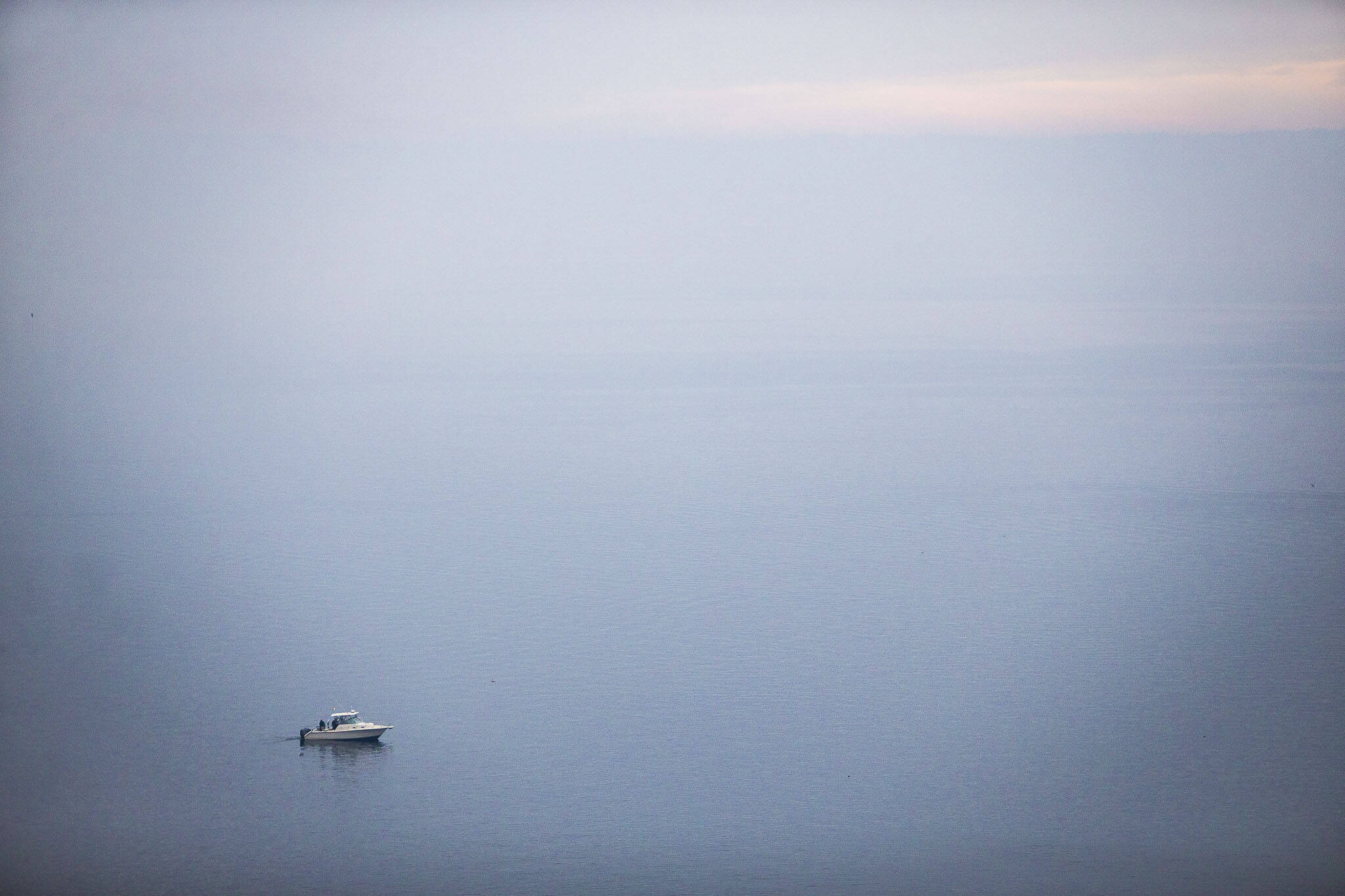 People fish on a boat along the edge of Possession Sound as the water is blanketed in smoke from the Bolt Creek fire and other wildfires burning in the Cascade range on Oct. 20, 2022, in Everett. (Olivia Vanni / The Herald)