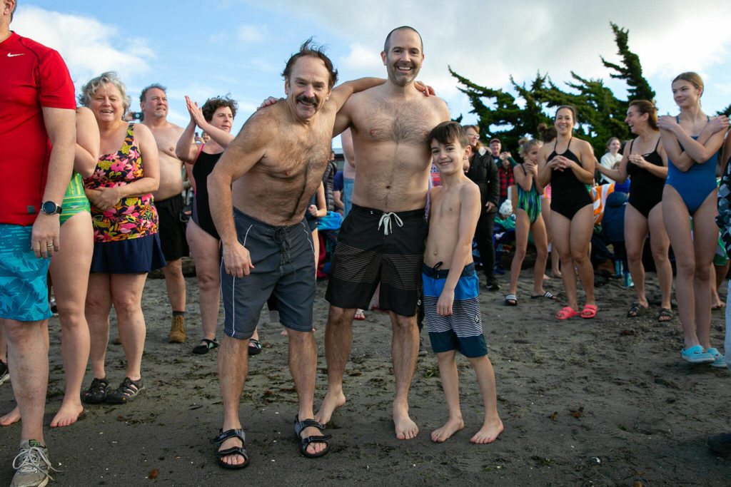 Three generations of Larson boys — grandpa Dan, father Chris, and 9-year-old Jack — take a moment for a photo before taking the plunge during the 2023 Edmonds Polar Bear Plunge on Sunday, Jan. 1, 2023, at Brackett’s Landing in Edmonds, Washington. The polar plunge is a long-standing tradition for the family. (Ryan Berry / The Herald)
