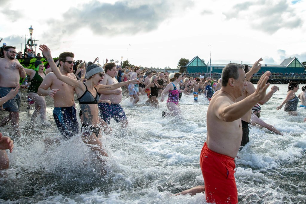 People sprint into the frigid waters of the Puget Sound to help ring in the new year during the 2023 Edmonds Polar Bear Plunge on Sunday, Jan. 1, 2023, at Brackett’s Landing in Edmonds, Washington. (Ryan Berry / The Herald)
