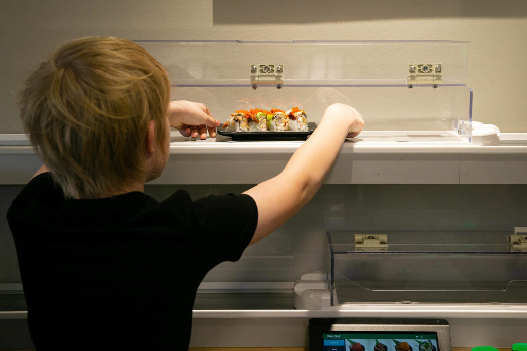 Levi Arneson, 12, grabs a roll from the monorail system next to his table at Sushi Hana on Jan. 5, in Lynnwood. (Ryan Berry / The Herald)
