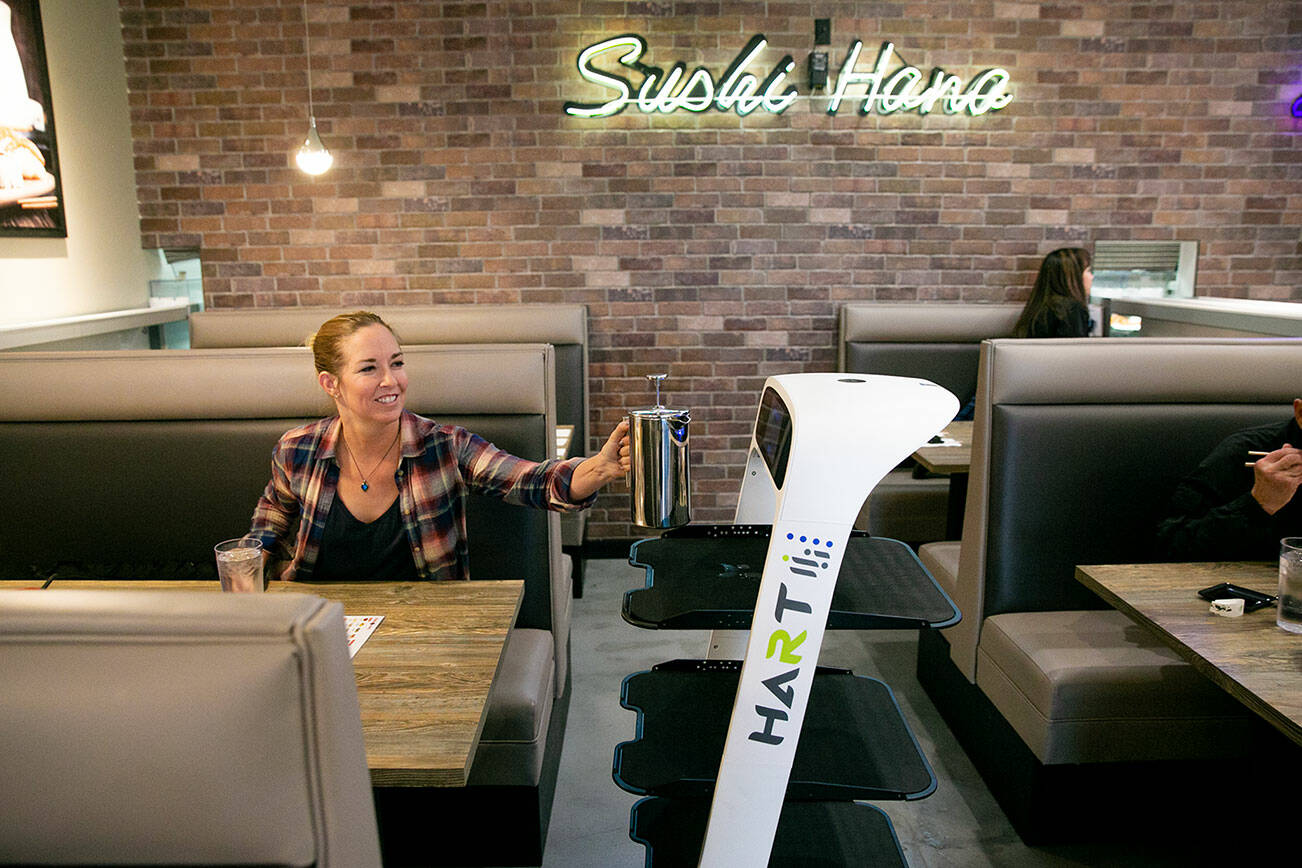 CarlaRae Arneson, of Lynnwood, grabs a tea press full of fresh tea from Peanut the server robot while dining with her 12-year-old son Levi at Sushi Hana on Thursday, Jan. 5, 2023, in Lynnwood, Washington. CarlaRae said she and her son used to visit the previous restaurant at Sushi Hana’s location and were excited to try the new business’s food. (Ryan Berry / The Herald)