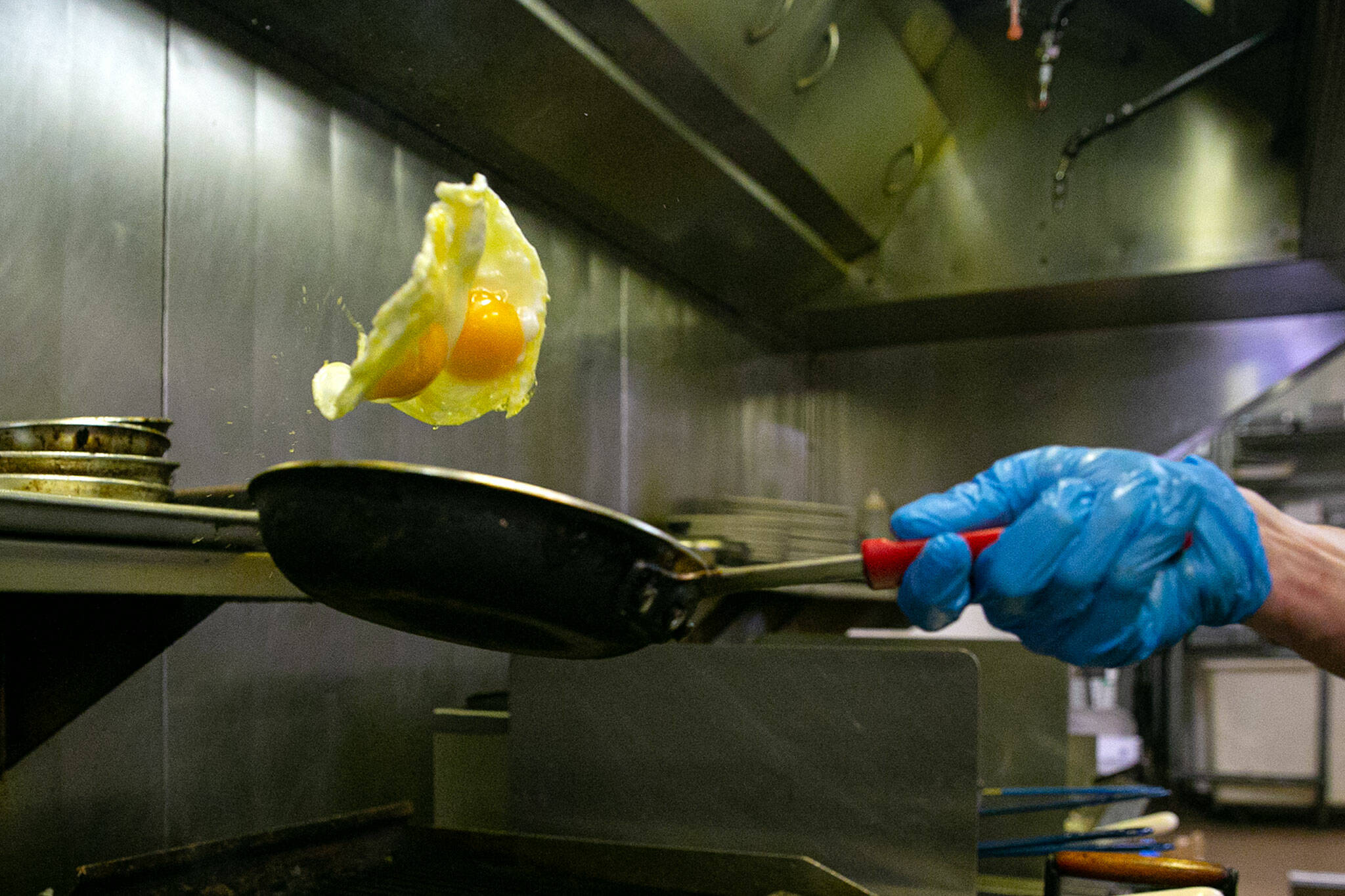 Line cook Scott McKenzie flips a pair of eggs while working during lunch service at Totem Family Diner on Saturday, in Everett. (Ryan Berry / The Herald)