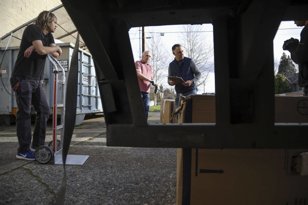 Store manager Dan Boston, 60, center, and store owner Jay Behar, 50, right, work to help unload a truck of recliners at Behar’s Furniture on Monday. Behar’s Furniture on Broadway in Everett is closing up shop after 60 years in business. The family-owned furniture store opened in 1963, when mid-century model styles were all the rage. Second-generation owner, Jay Behar says it’s time to move on. (Annie Barker / The Herald)
