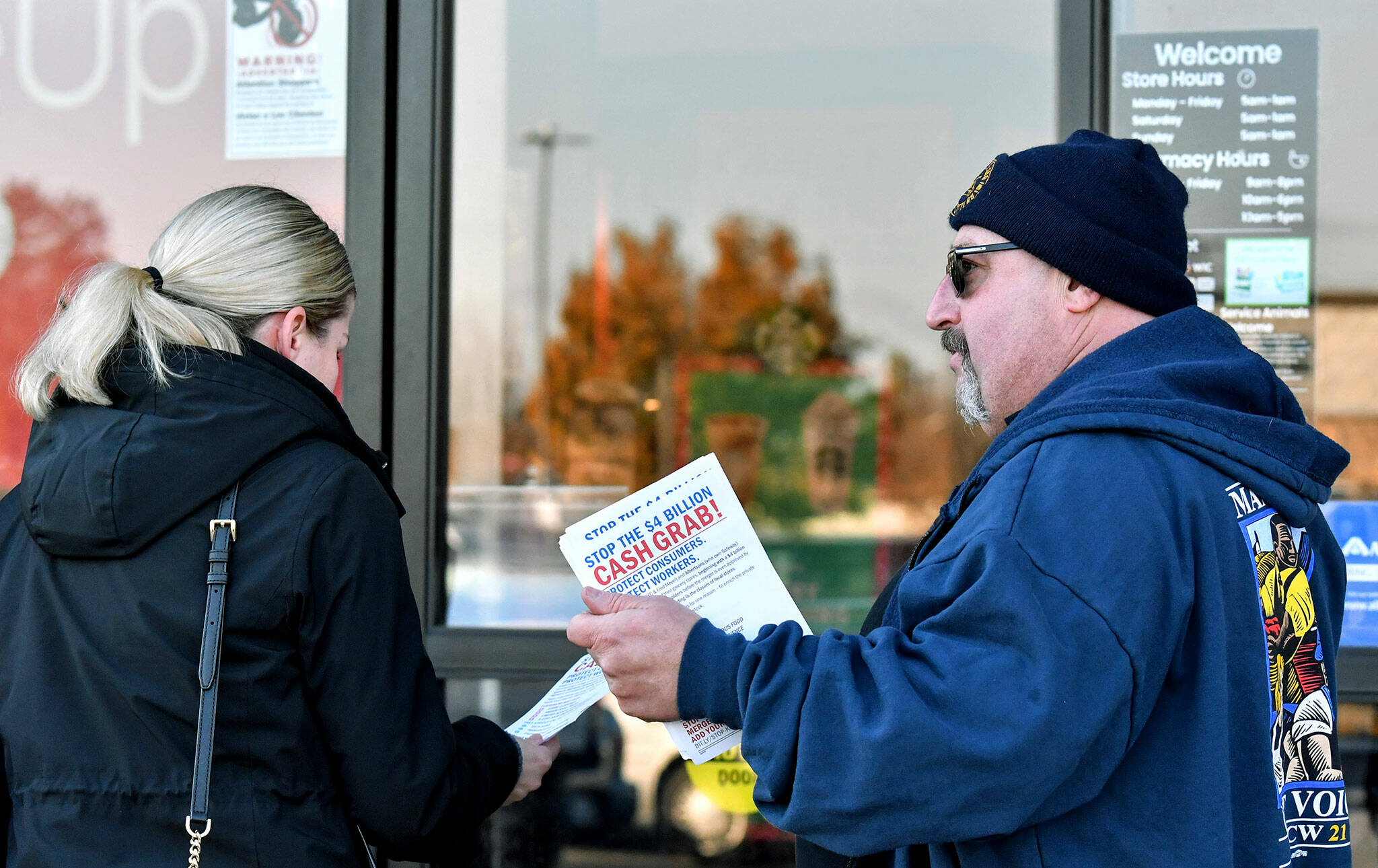 Kevin Flynn, right, a meat-cutter with the Marysville Albertsons, hands a leaflet to a shopper during an informational campaign on Nov. 9, 2022. Flynn was one of about a dozen grocery store workers handing out leaflets to shoppers about the proposed merger between Albertsons and Kroger. (Mike Henneke / The Herald)