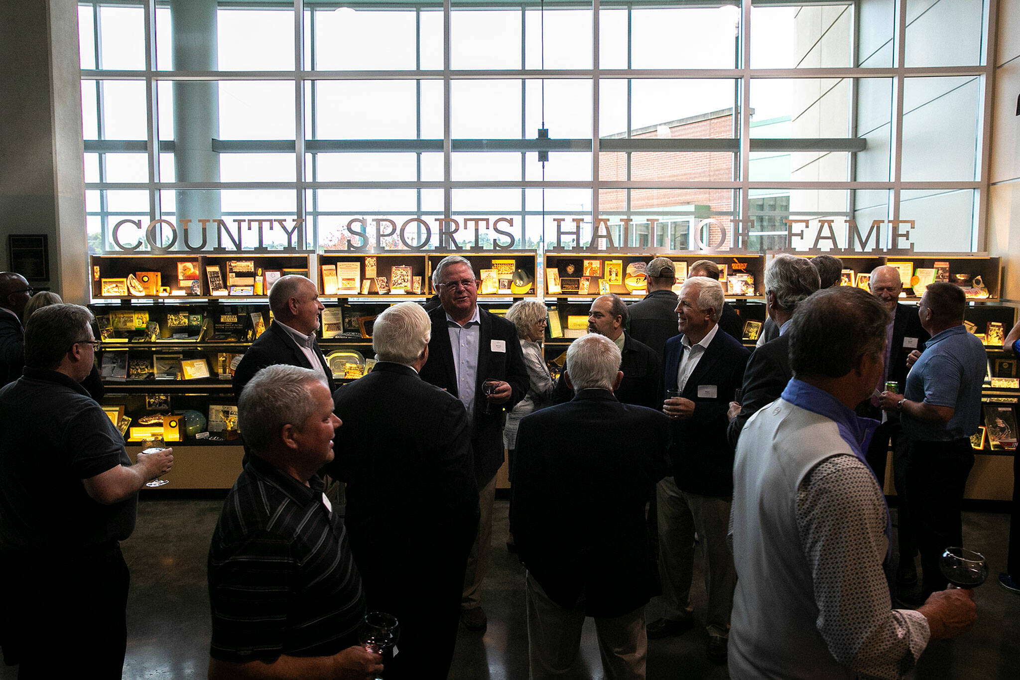 People gather in front of the Snohomish County Sports Hall of Fame display case during the 2022 Hall of Fame banquet on Sep. 28, 2022, at the Edward D. Hansen Conference Center in Everett. (Ryan Berry / The Herald)