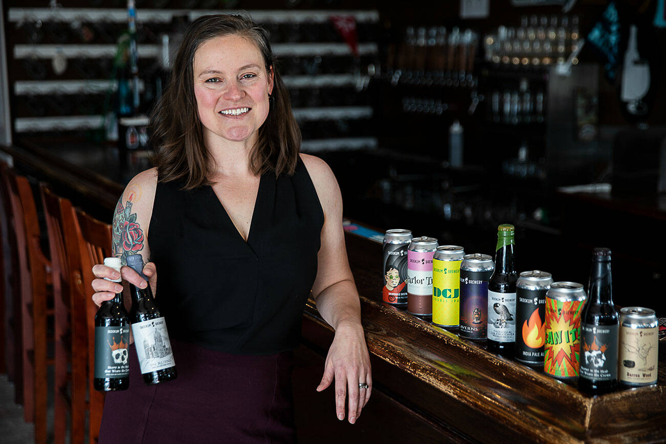 Designer Alyson Osborn with a handful of beer labels she illustrated and designed for Skookum Brewery on Monday, Jan. 9, 2023 in Lynnwood, Washington. (Olivia Vanni / The Herald)