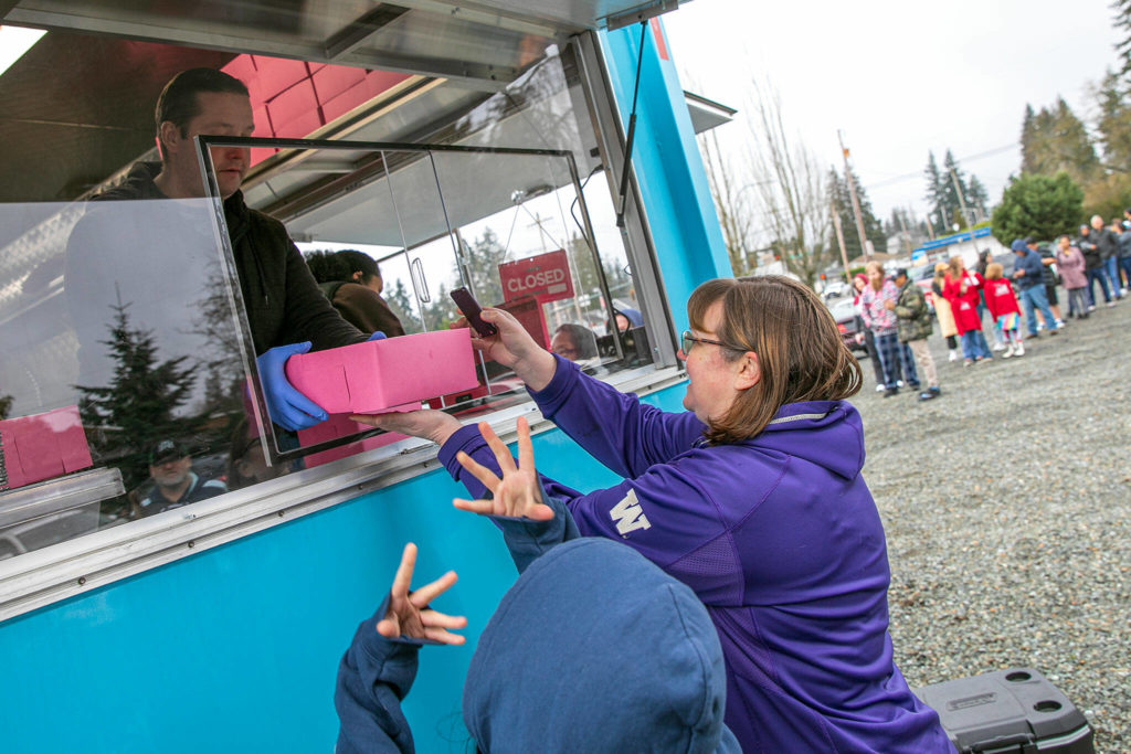Idamae Nguyen collects her order of malasadas from Brandon Hamilton for herself and her children Kailene, 11, and Jacob, 7. The Nguyens arrived half an hour early and claimed the third spot in line. (Ryan Berry / The Herald)
