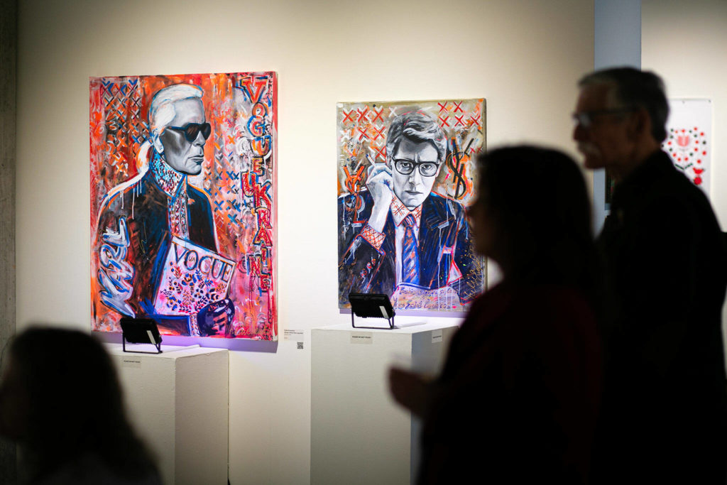 People watch a video installation while standing near a pair of paintings by Yuliia Kravchenko during a public event highlighting the For Ukraine: Art of Freedom exhibit at the Schack Art Center on Saturday, in downtown Everett. (Ryan Berry / The Herald) 
