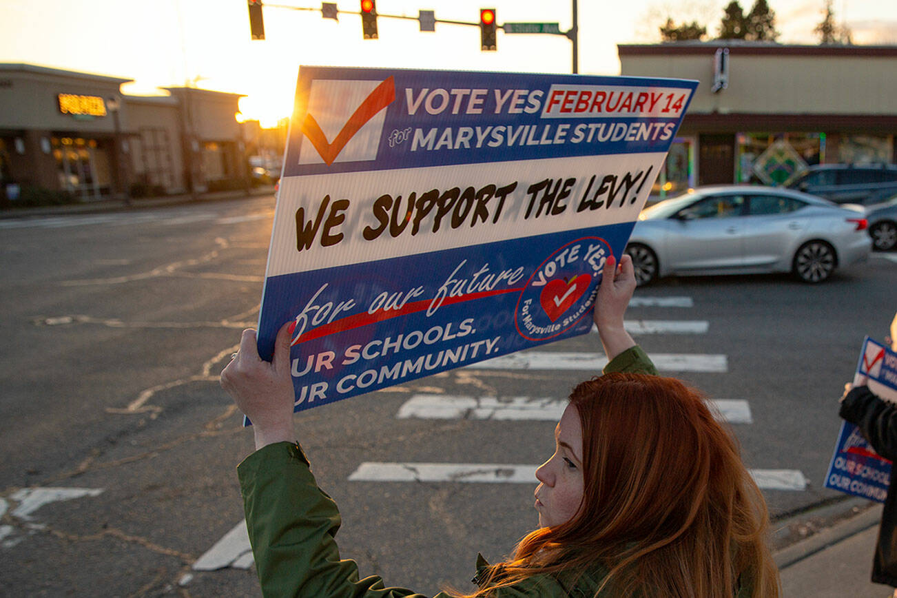 Community advocate and former state representative Emily Wicks waves signs at the corner of 4th and State along with Christie Ryba-Johnson and Matt Ruskowski, both employees at Marysville School District, in support of a school levy being voted on on Tuesday, Feb. 14, 2023, in Marysville, Washington. (Ryan Berry / The Herald)