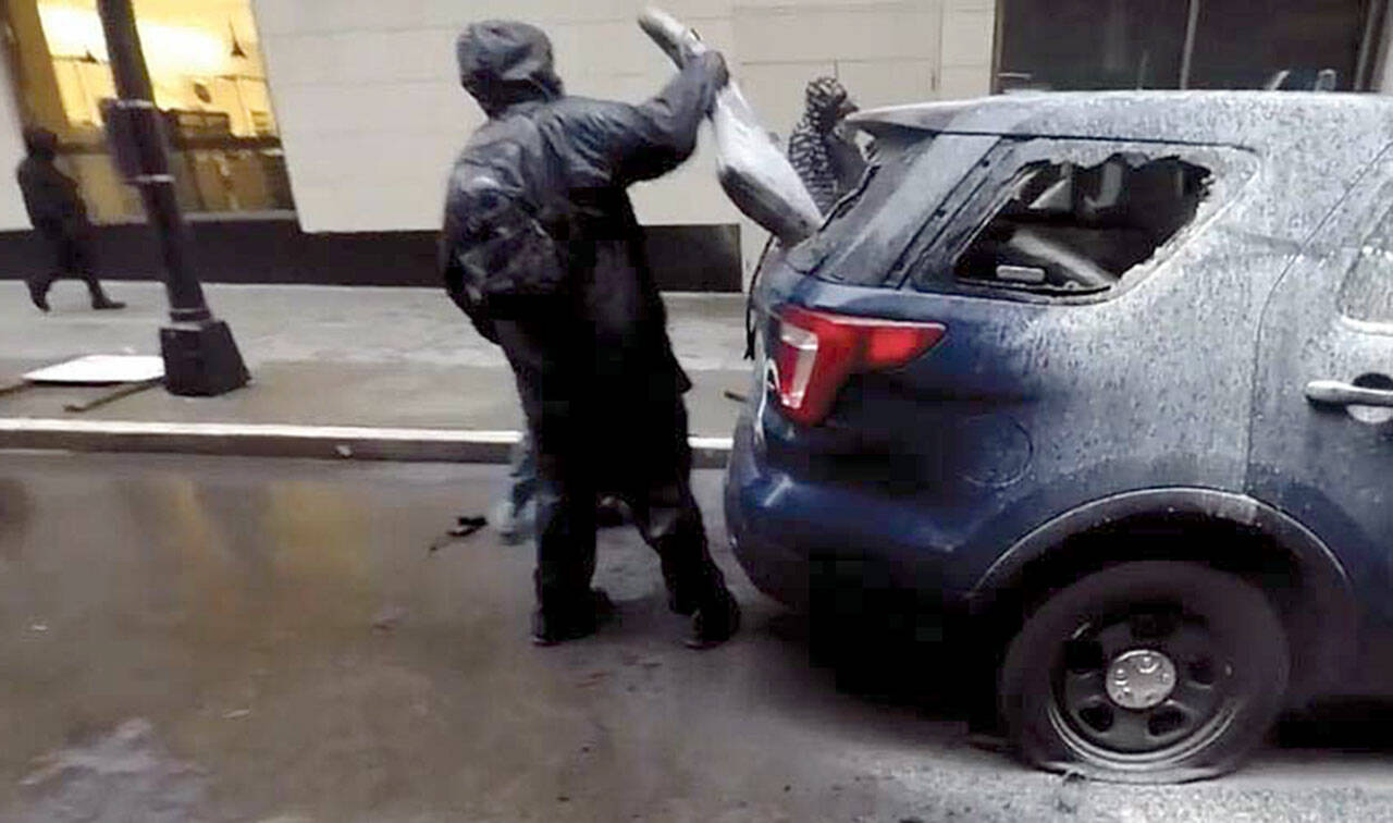 A suspect removes a rifle bag from a broken rear window of a Seattle police car on May 30 in downtown Seattle. An Everett man, Jacob D. Little, 24, has been charged with the theft of the high-powered rifle stolen from the car. This image is from the criminal complaint filed in U.S. District Court. 20200904