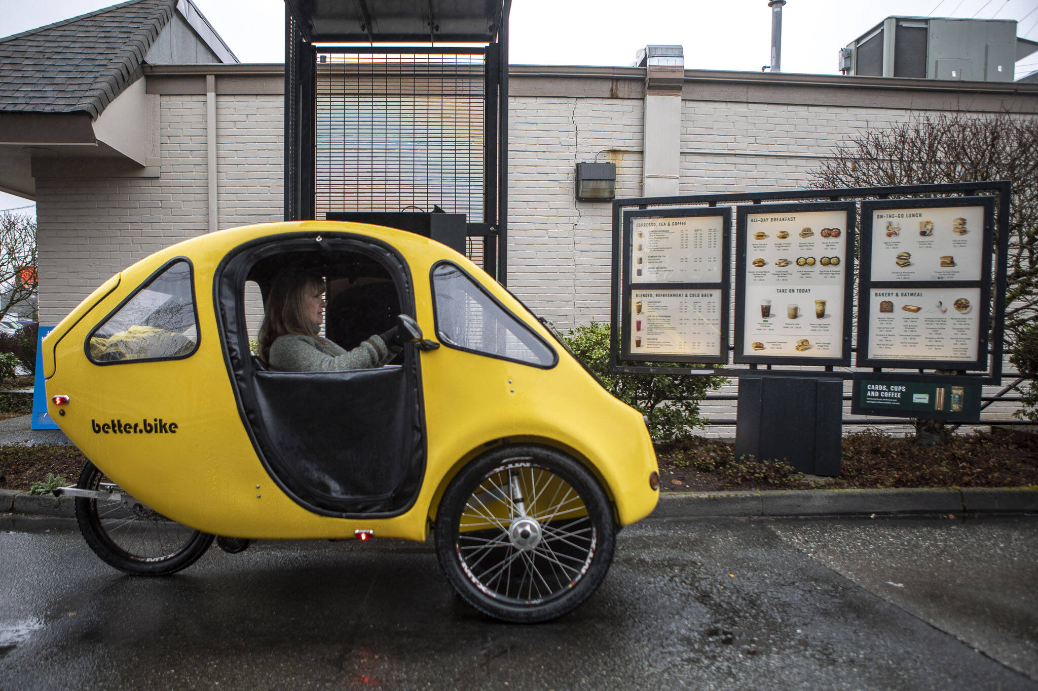 Paula Townsell pedals a PEBL microcar electric bike at an Everett drive-thru. She uses the PEBL to go around town, do errands and get exercise. It goes 100 miles on a charge. Townsell and her husband, Chris Glans, bought the PEBL used off Craigslist in 2020 from a seller in Anacortes for $7,900. PEBL is made by the Massachusetts company BetterBike. (Annie Barker / The Herald)