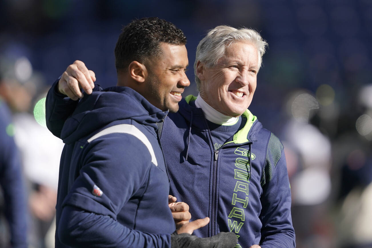 Seattle Seahawks head coach Pete Carroll, right, throws his arm around injured quarterback Russell Wilson as they walk on the field before an NFL football game against the Jacksonville Jaguars, Sunday, Oct. 31, 2021, in Seattle. (AP Photo/Ted S. Warren)