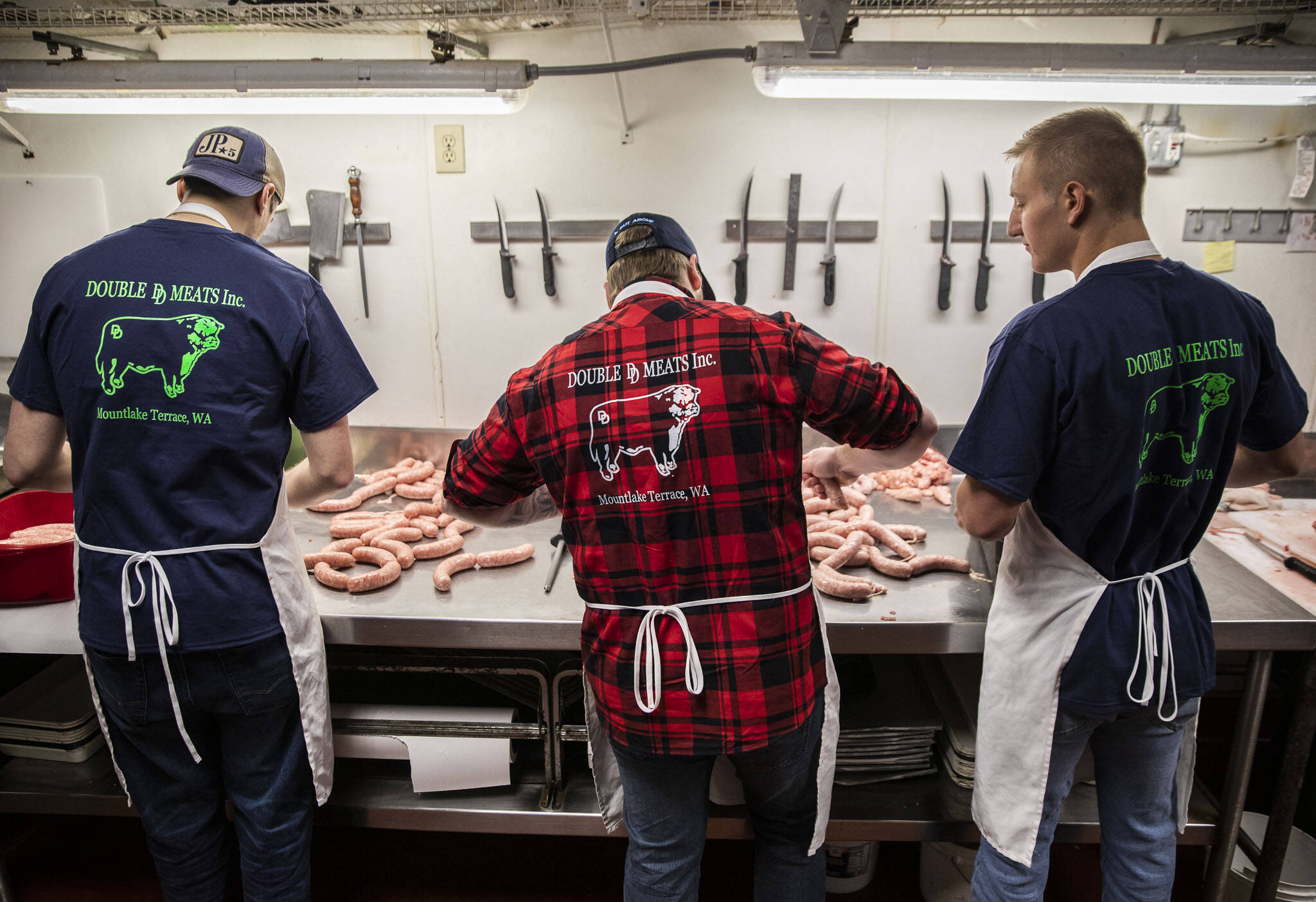 Logan Leadley, Kyle Thies and Jeremy Nygard tie sausages at Double DD Meats in Mountlake Terrace, Washington. (Olivia Vanni / The Herald)