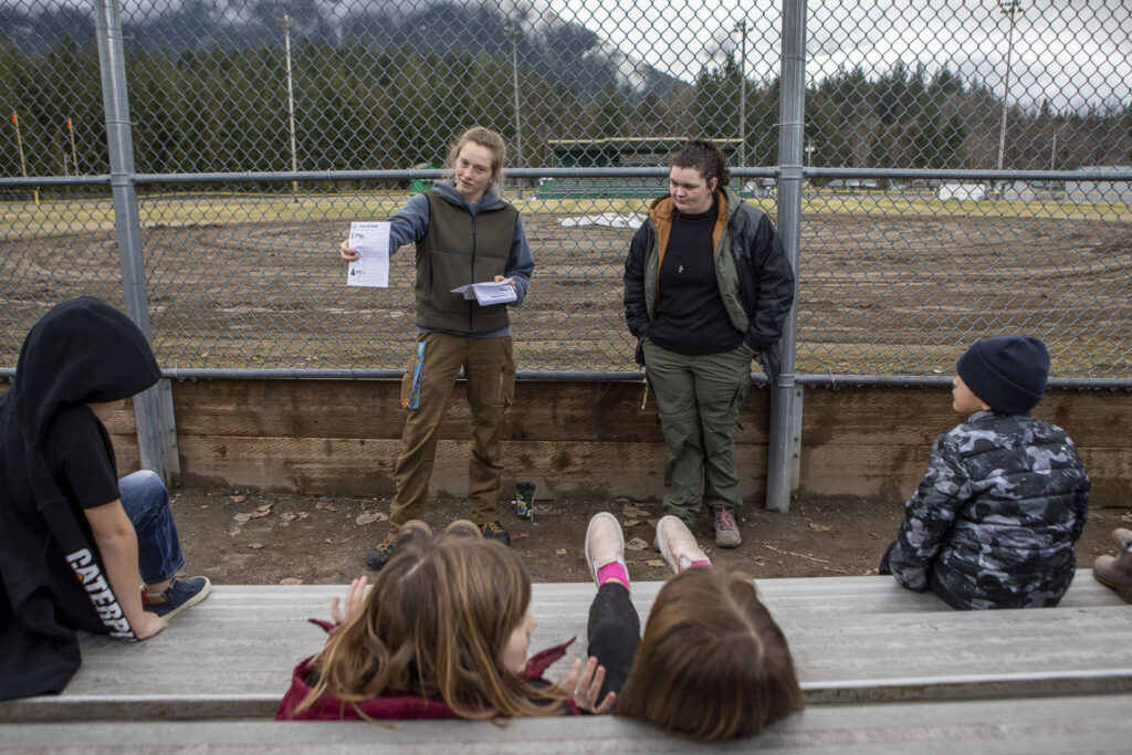 Instructors Hannah Dreesbach, left, and Bailey Huff, right, discuss how to identify trees near Darrington Elementary School on Feb. 17 in Darrington. Environmental and outdoor education lessons are woven throughout the in-school and after-school activities in this small community, thanks to the Glacier Peak Institute. The non-profit arose from community concerns in the wake of the Oso landslide disaster. (Annie Barker / The Herald)
