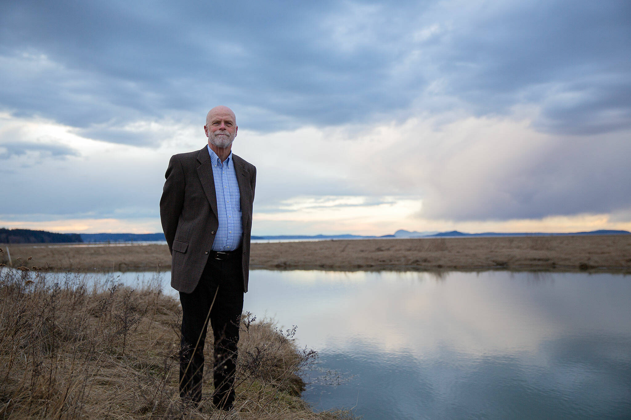 Stanwood Mayor Sid Roberts stands in the tidal zone of Skagit Bay where the Stillaguamish River meets the ocean on Tuesday, March 7, 2023, on the west end of Stanwood, Washington. When this land swells with water during high tides, a more-than-100-year-old dike is all that protects downtown Stanwood from potentially catastrophic flooding. The city of Stanwood has secured millions in grant money to begin working towards a fix for the 4-mile earthen wall. (Ryan Berry / The Herald)