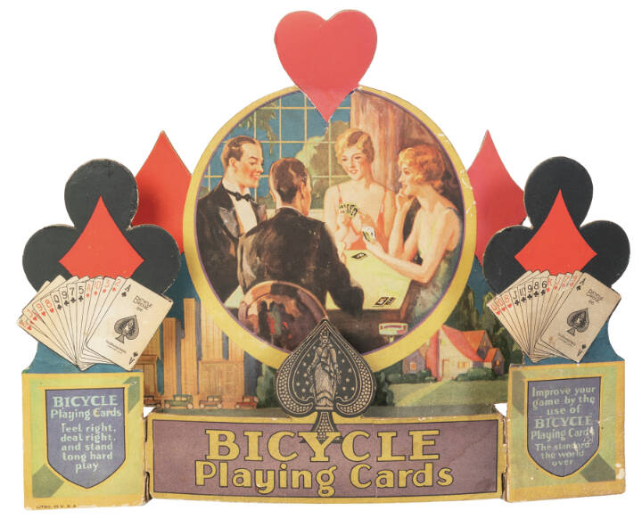 When advertisements include pictures of people, their clothing and hairstyles can help date the item. This store display for Bicycle Playing Cards is from about 1930.
