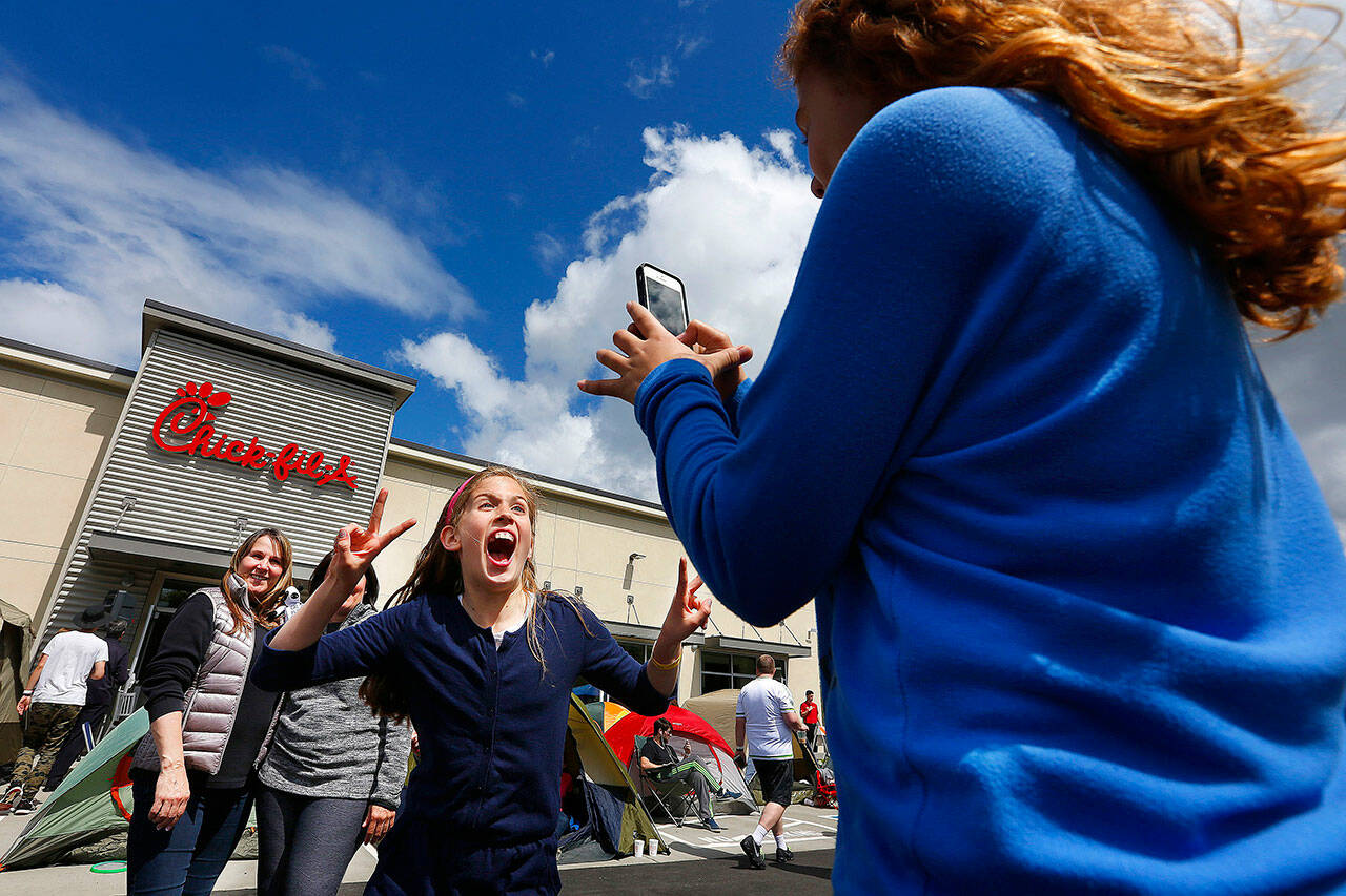 Chloe Charles (center) jumps into the middle of a picture being taken by Jada Summers of the girls’ respective mothers, Renee Charles (left) and Debbie Summers during the grand opening of Chick-Fil-A’s first Lynnwood location on May, 6 2015. (Mark Mulligan / The Herald)