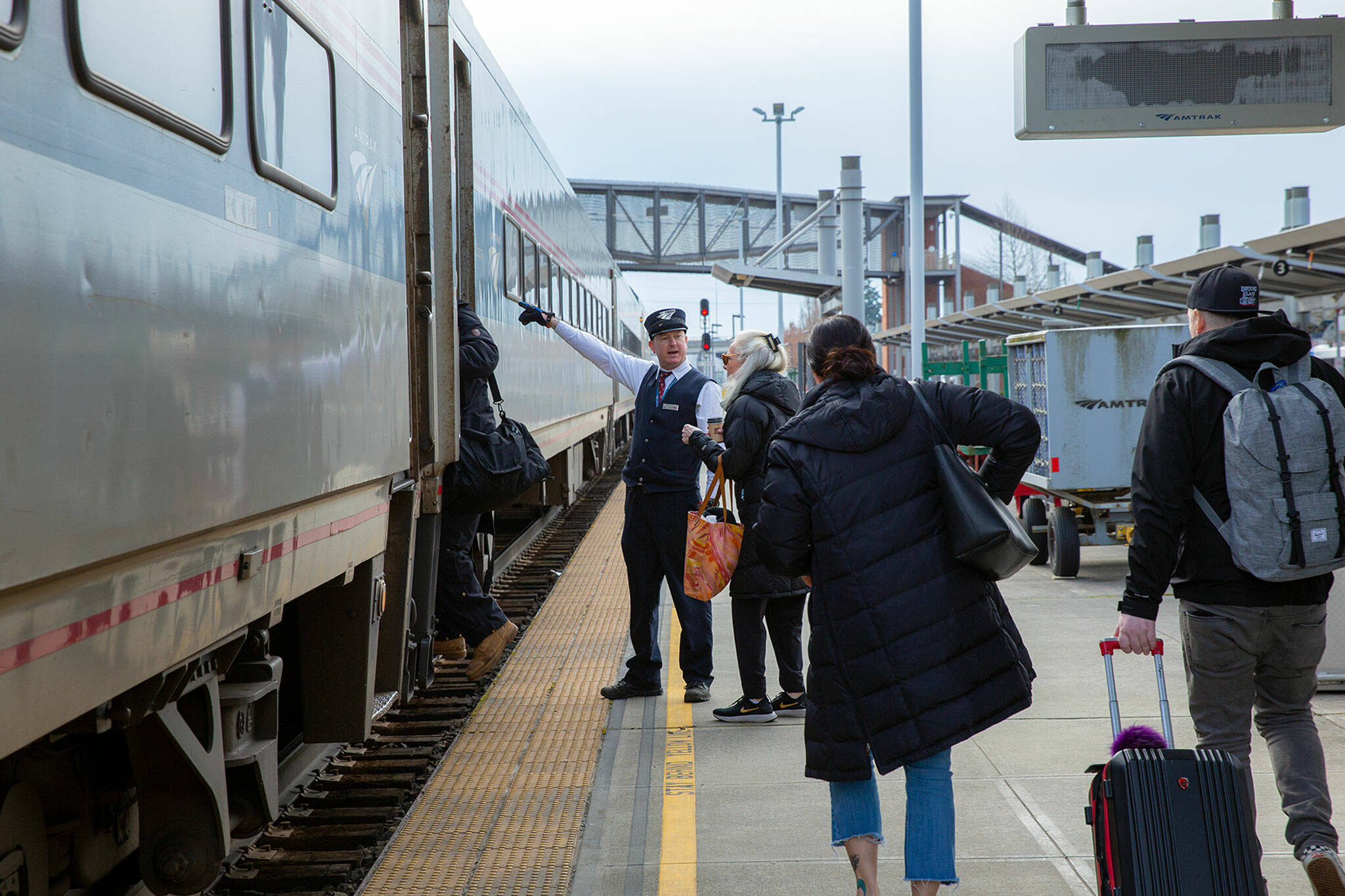 A conductor guides travelers onto Amtrak Cascades train 517 from Vancouver to Portland as it stops through Everett Station Thursday. (Ryan Berry / The Herald)