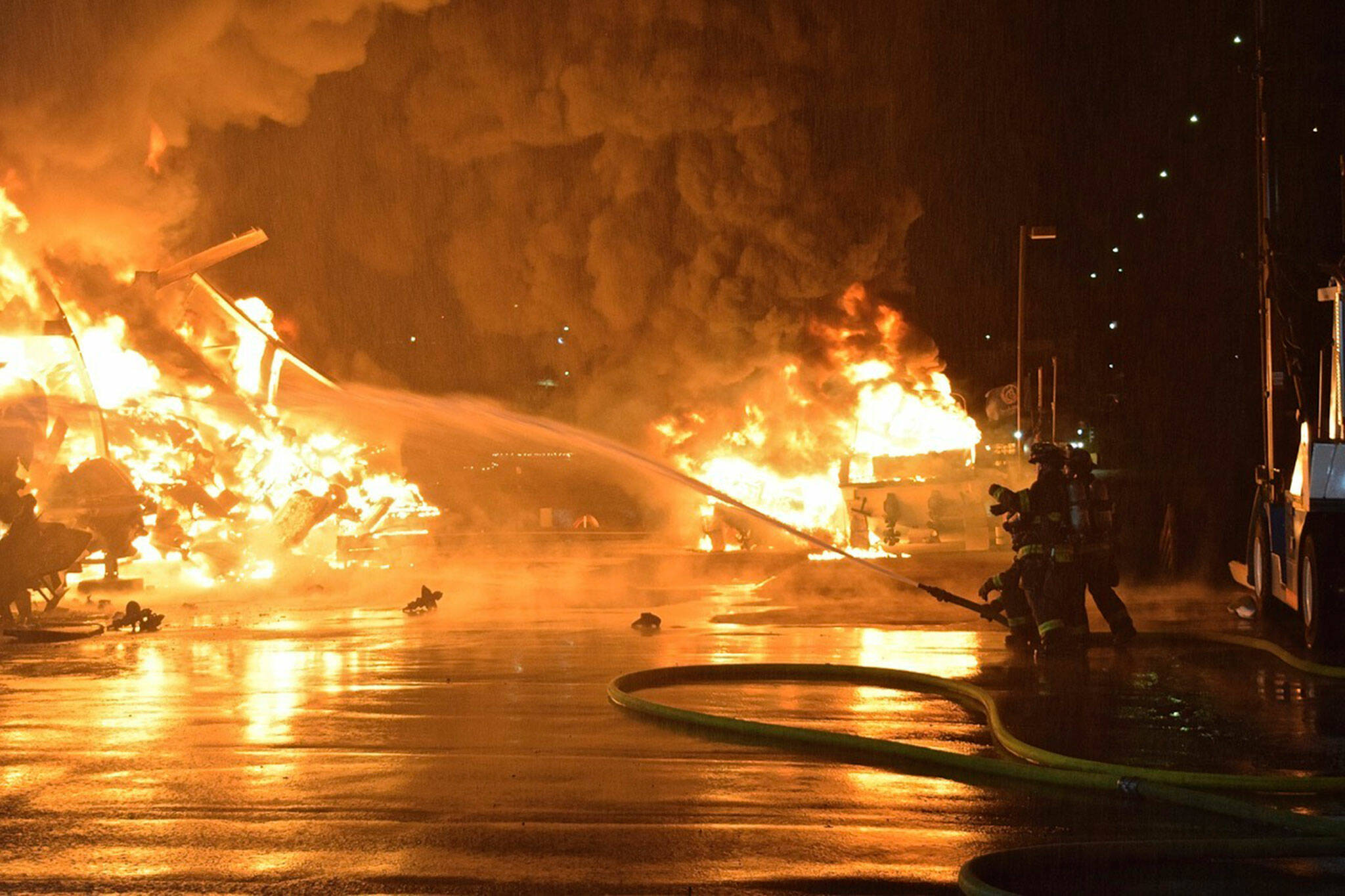 Firefighters in Seattle douse flames at a marina on Lake Union, near the city’s University District, early on Wednesday, March 22, 2023. The fire burned 30 boats on a dry-rack storage facility, and a man found hiding in one vessel was arrested for investigation of arson, authorities said. (John Odegard via AP)