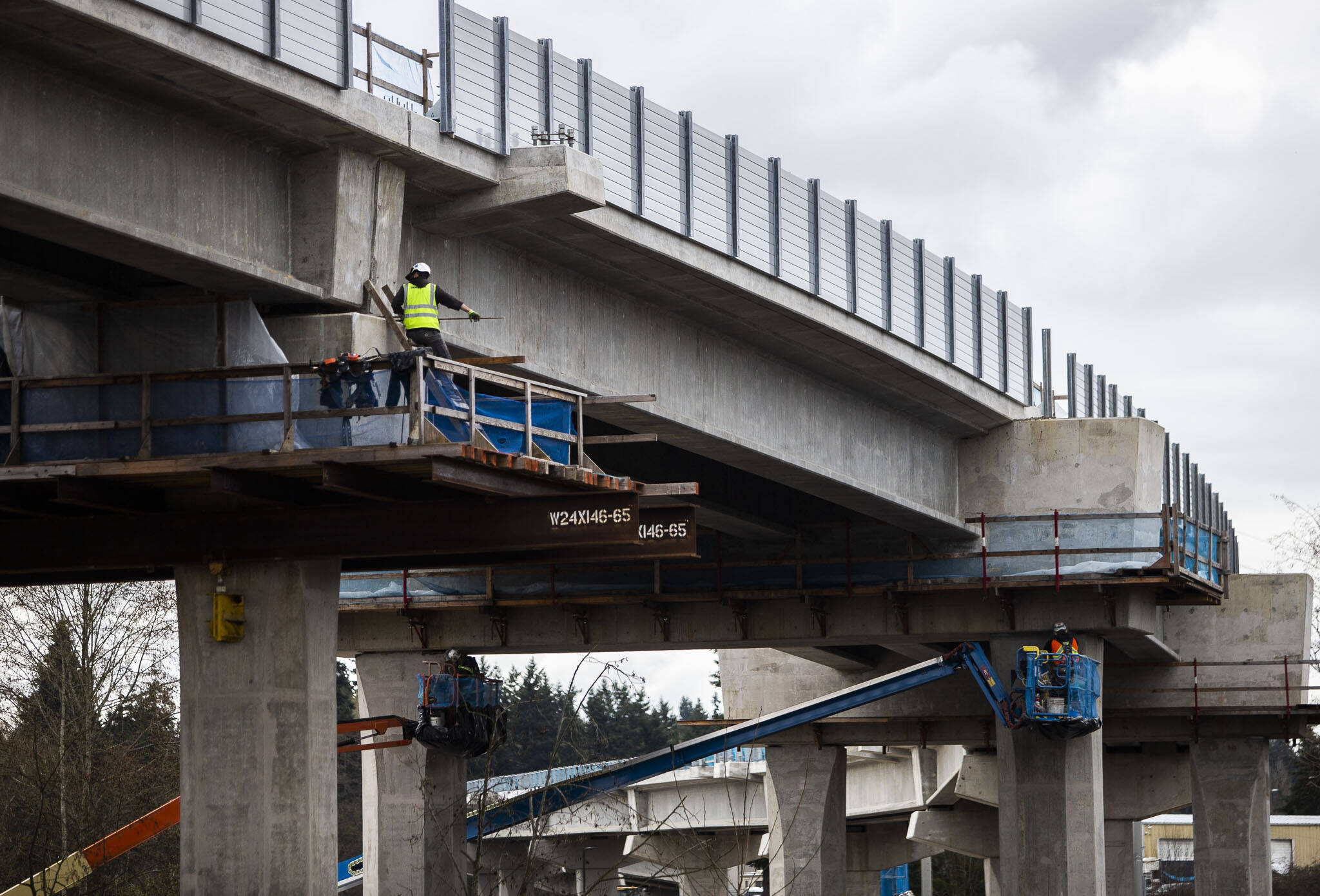Construction workers walk along the underside of Sound Transit’s Link light rail tracks in March 2022 in Lynnwood. (Olivia Vanni / The Herald file photo)