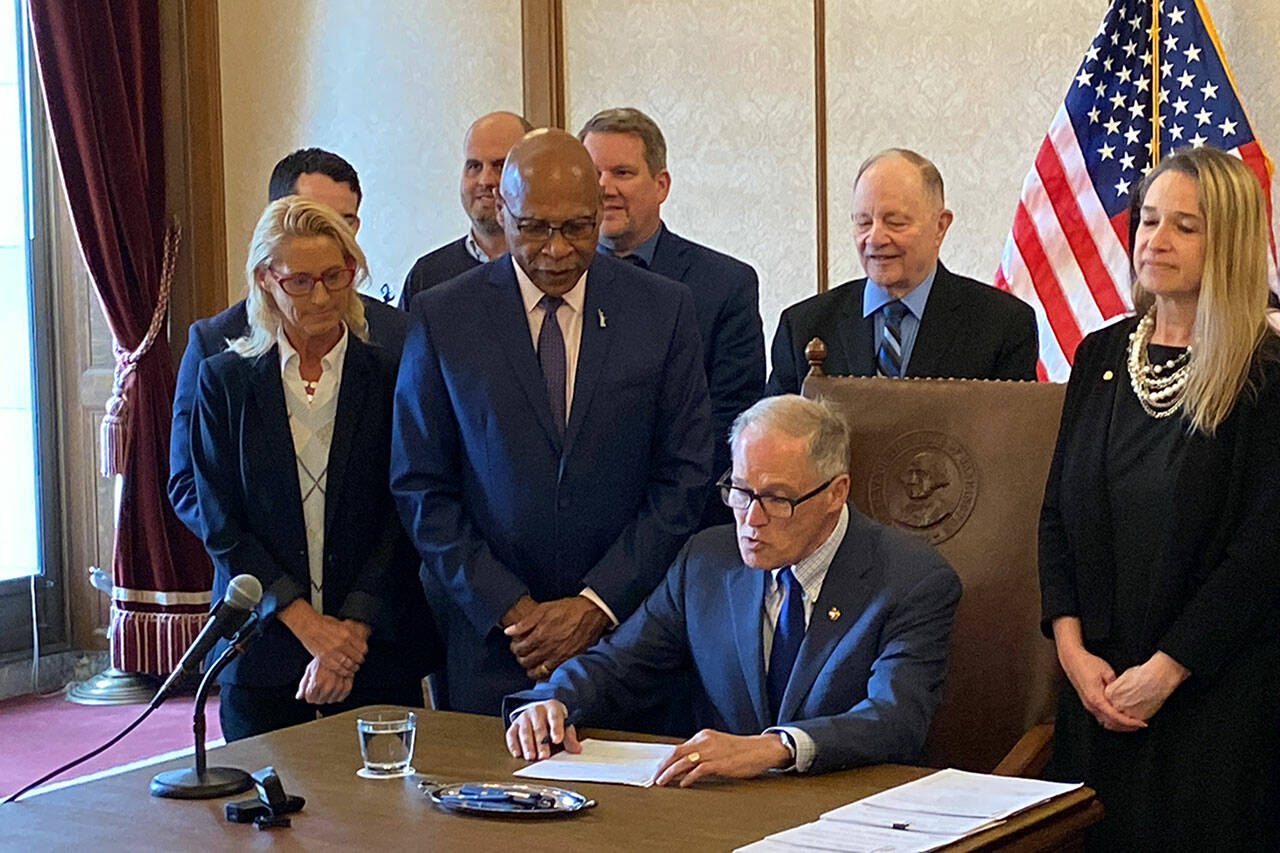 Gov. Jay Inslee signed legislation Thursday to add a ninth judge to the Snohomish County District Court. Sen. John Lovick, D-Mill Creek, who sponsored the bill, and Presiding District Court Judge Jennifer Rancourt look on. (Jerry Cornfield / The Herald)