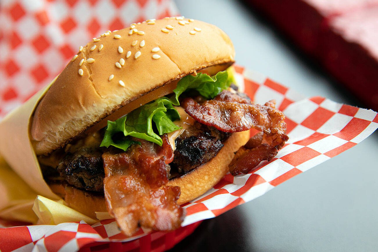 Nick’s Jr.’s peanut butter bacon burger glistens in the light on Friday, March 31, 2023, at the restaurant in Everett, Washington. The burger consists of a seasoned patty with melty Skippy Super Chunk peanut butter, two bacon slices, lettuce, tomato and mayo on a toasted sesame seed bun.(Ryan Berry / The Herald)