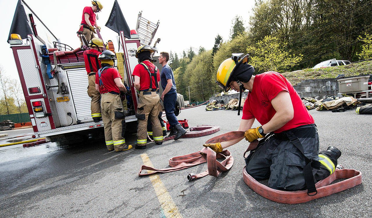 After a day of learning to fight fires, Everett firefighter recruit Chau Nguyen flakes a hose as other recruits load the hoses onto a fire truck at a training facility Thursday, April 19, 2018, on S. Machias Road in Snohomish. (Andy Bronson / The Herald)
