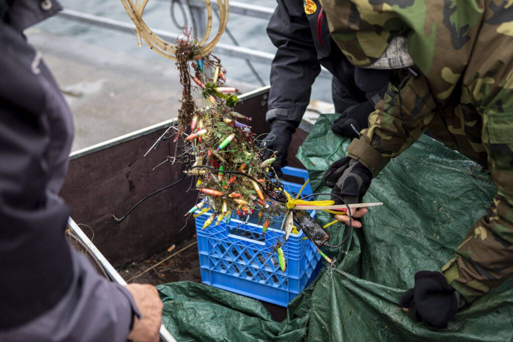 A basket full of lures and other finds is examined during an underwater scuba maintenance event at the Edmonds Fishing Pier in Edmonds, Washington on Sunday, April 2, 2023. (Annie Barker / The Herald)
