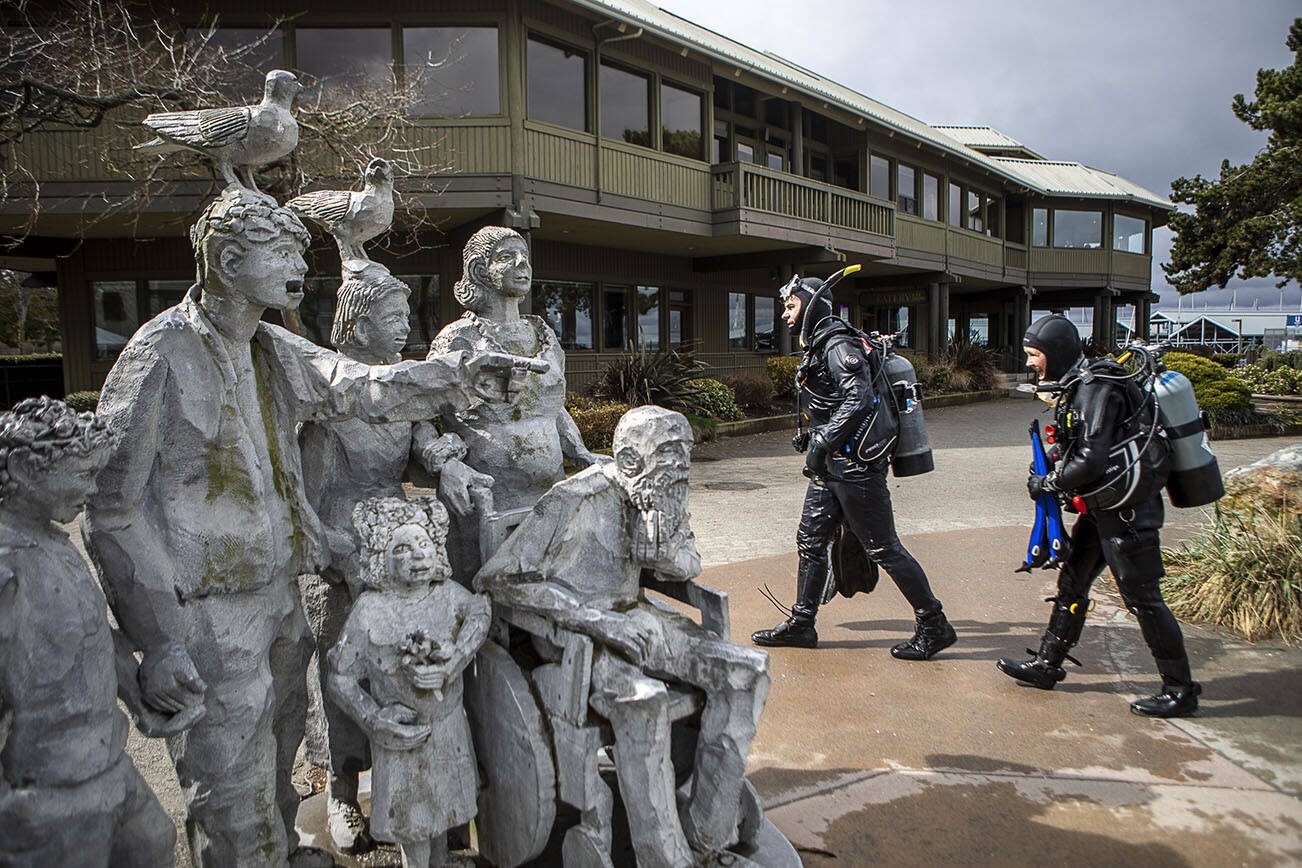 Kelly Moore, 39, left, and Vanessa Walsh, 55, right, make their way back on land during an underwater scuba maintenance event at the Edmonds Fishing Pier in Edmonds, Washington on Sunday, April 2, 2023.  (Annie Barker / The Herald)