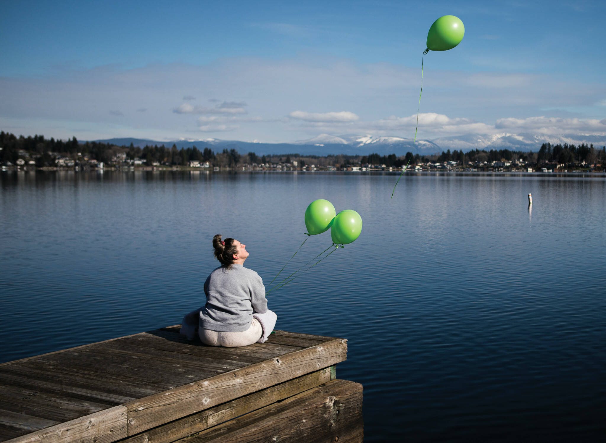 Ashley Olson releases green balloons from the dock at Davies Beach on Lake Stevens in memory of her brother, Joey Mell, who overdosed a year earlier. Green was Mells favorite color and Olson describes her brother as gorgeous and a real thrill seeker due to his job as a highline tree trimmer. (Photo by Olivia Vanni)