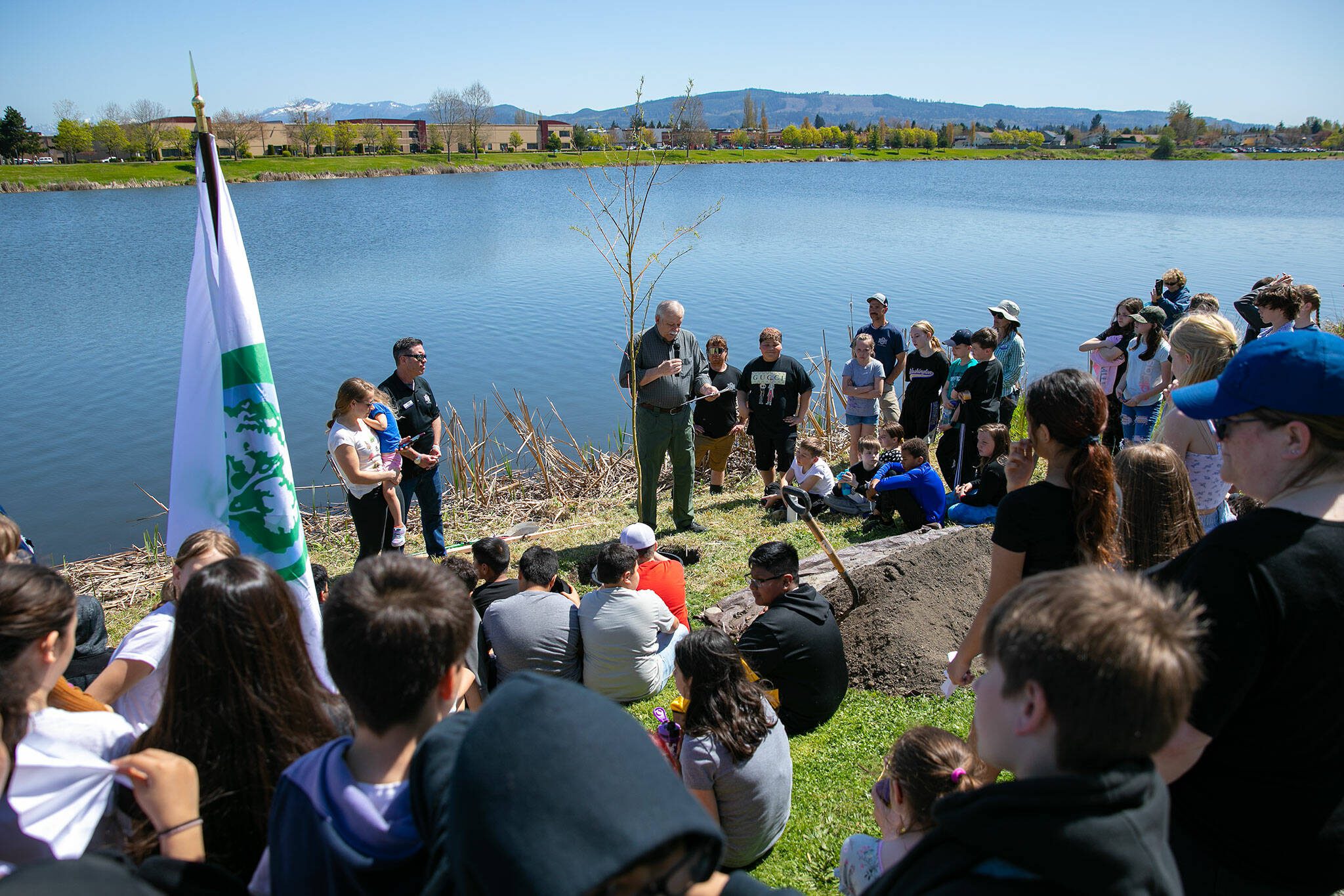 Freylands Elementary students gather around as Monroe Mayor Pro Tem Ed Davis welcomes everyone to an Arbor Day celebration at Lake Tye Park on Friday, April 28, 2023, in Monroe, Washington. (Ryan Berry / The Herald)
