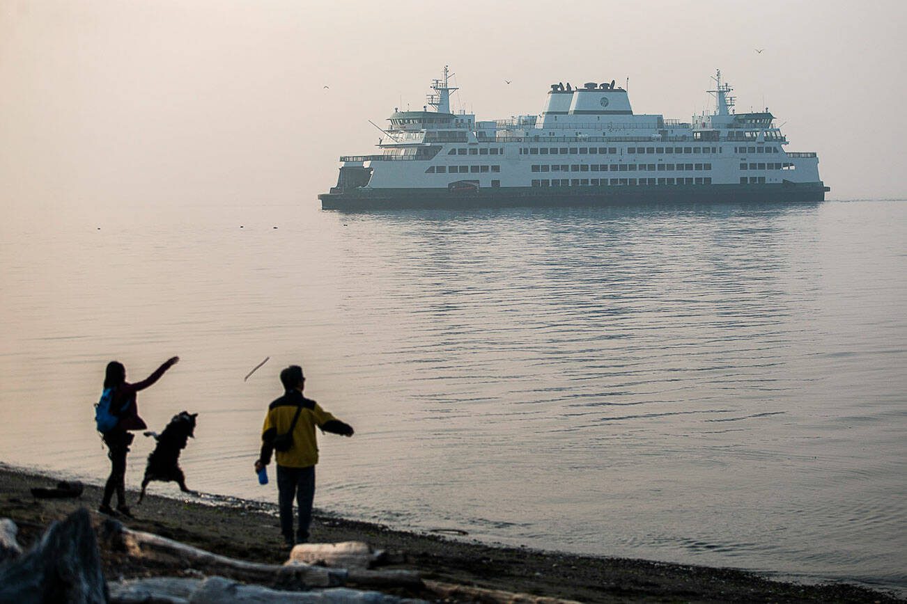 People throw sticks for their dog along Edgewater Beach while a ferry emerges from smoke covering Possession Sound on Wednesday, Oct. 19, 2022 in Mukilteo, Washington. (Olivia Vanni / The Herald)