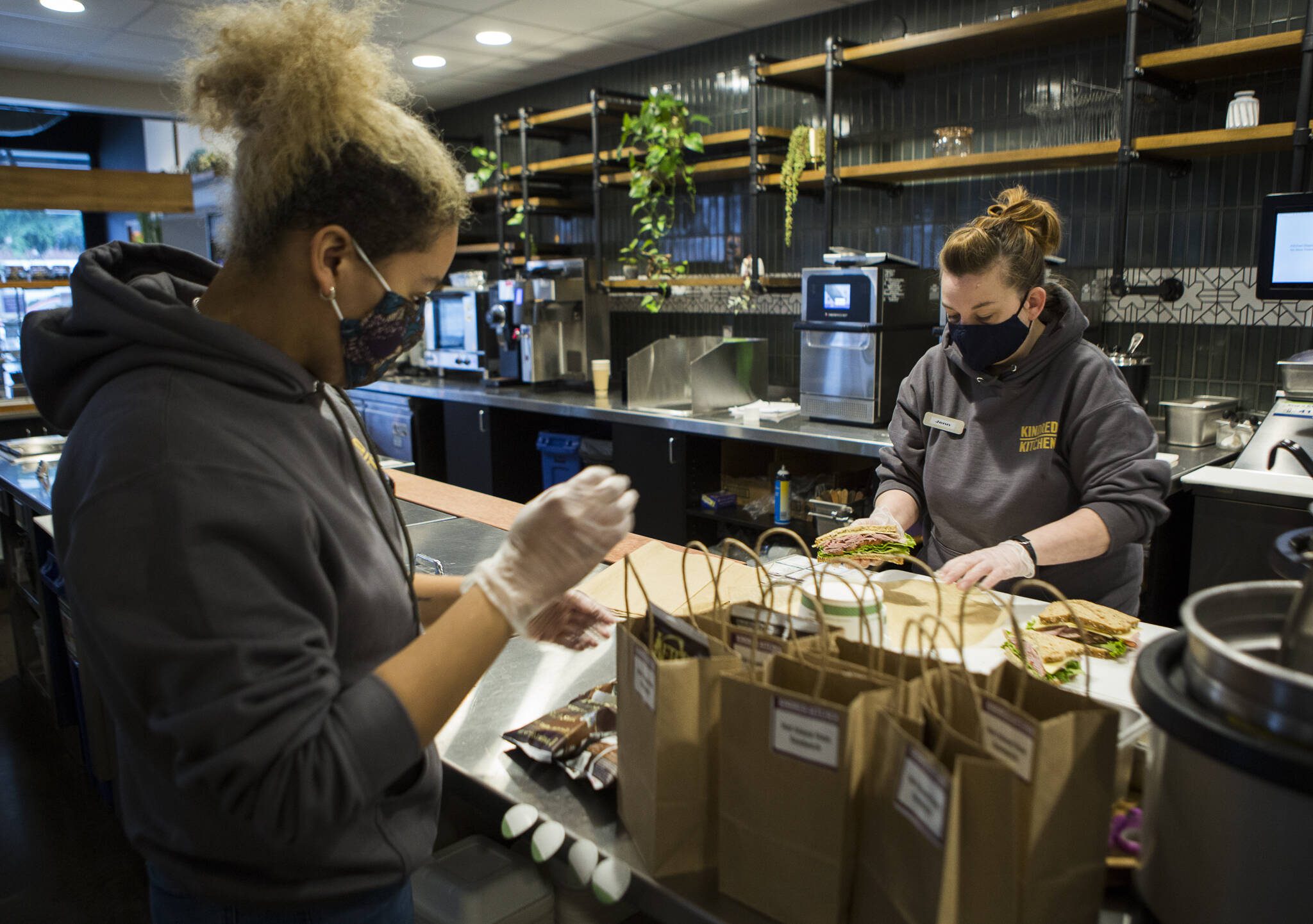 Shianne Shelton, left, and Jennifer Smith, right, prep sandwich lunches at Kindred Kitchen to be delivered to the volunteers the the Arlington Airport COVID-19 vaccination site on Friday, Feb. 12, 2021 in Everett, Washington. (Olivia Vanni / The Herald)