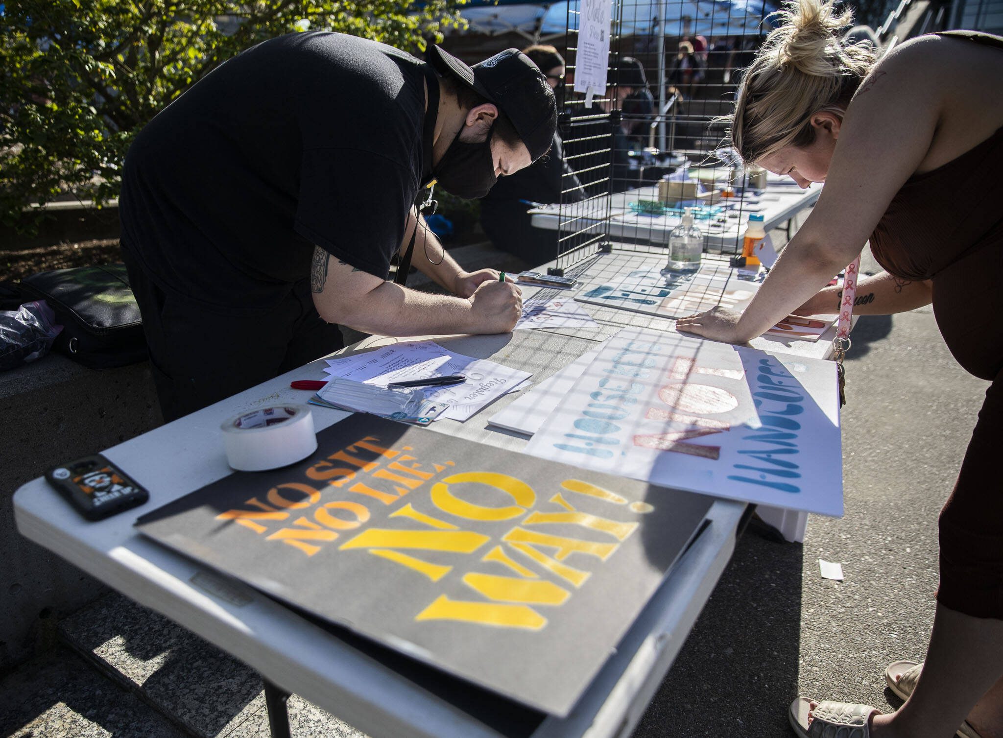 Ruben Trujillo, left and Sarah Bates, right, work on signs in protest of the “no sit, no lie” expansion on Wednesday, May 3, 2023 in Everett, Washington. (Olivia Vanni / The Herald)