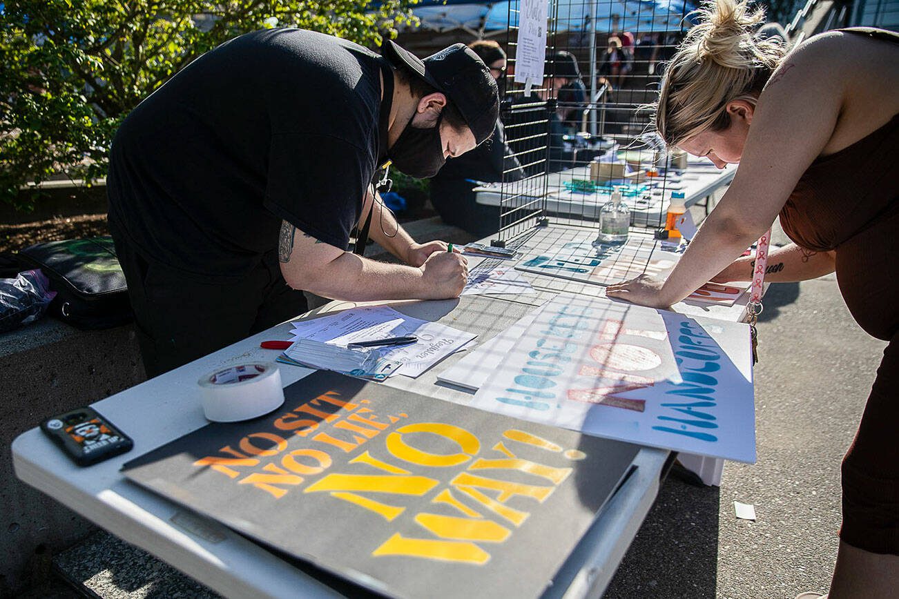 Ruben Trujillo, left and Sarah Bates, right, work on signs in protest of the “no sit, no lie” expansion on Wednesday, May 3, 2023 in Everett, Washington. (Olivia Vanni / The Herald)