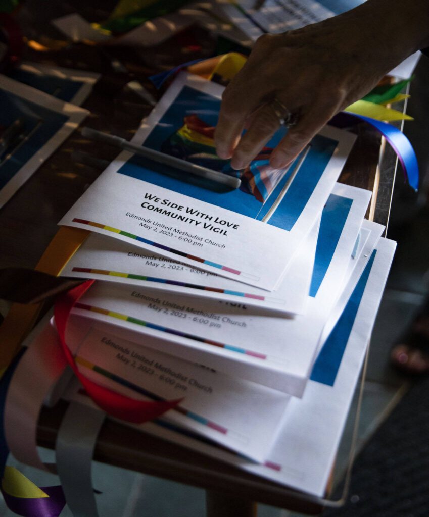 “We Side With Love” programs are handed out with multi-colored ribbons as people begin to file in to the vigil held at Edmonds United Methodist Church on Tuesday, May 2, 2023 in Edmonds, Washington. (Olivia Vanni / The Herald)
