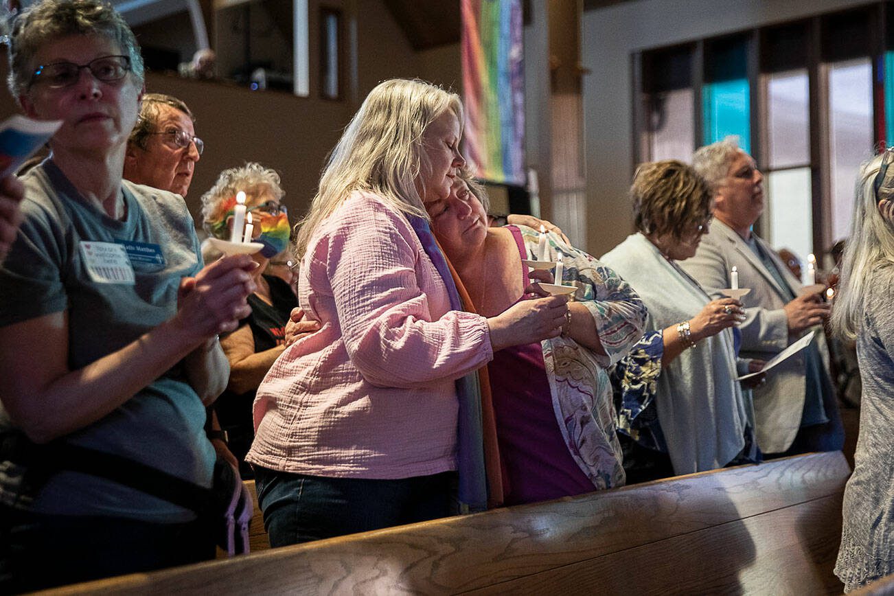 Anne Long, left, and Stacy Miller, right, embrace while singing "We Shall Overcome" during a vigil held to support the LGBTQIA+ community in response to the recent hate-filled incidents at two regional churches on Tuesday, May 2, 2023, in Edmonds, Washington. Long, from Seattle and Miller, from Ferndale, both felt it was important to attend to “show support." (Olivia Vanni / The Herald)