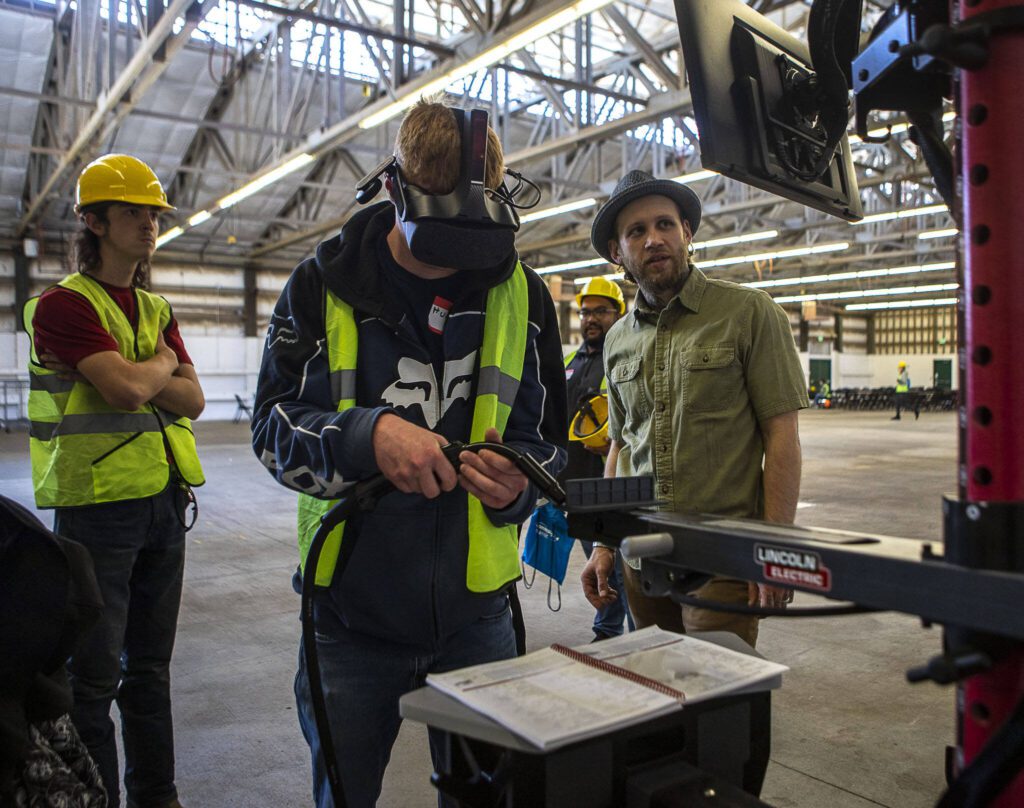 Hunter Mattson, center, is guided by Blake Horton, right, on a virtual welding simulation during a trade fair at the Evergreen State Fairgrounds in Monroe, Washington on Wednesday, May 3, 2023. High school kids learned about various trades at the event. (Annie Barker / The Herald)
