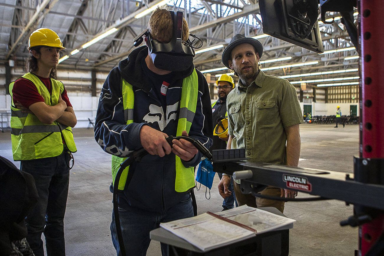 Hunter Mattson, center, is guided by Blake Horton, right, on a virtual welding simulation during a trade fair at the Evergreen State Fairgrounds in Monroe, Washington, on Wednesday, May 3, 2023. High school kids learned about various trades at the event. (Annie Barker / The Herald)