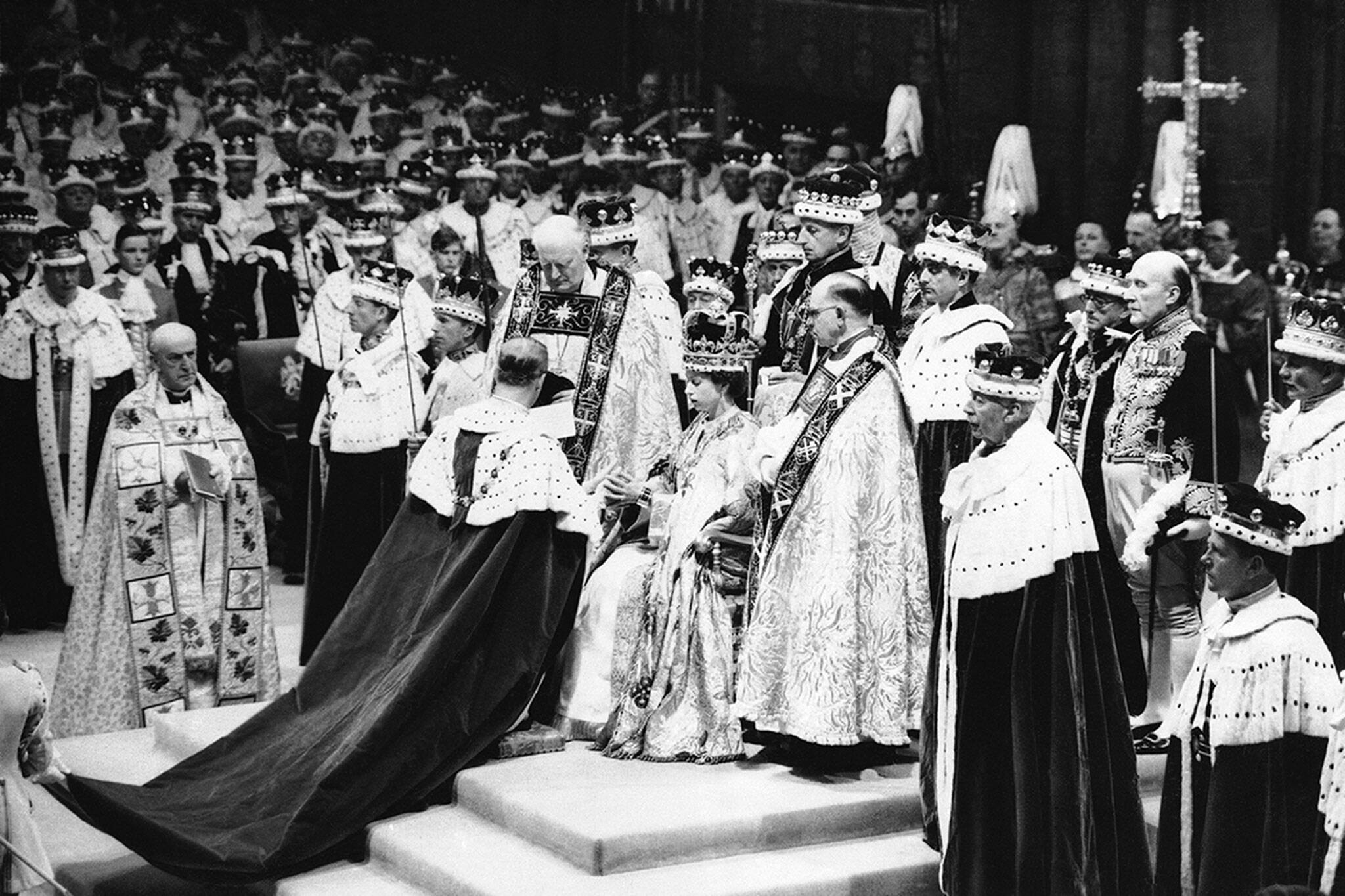 Surrounded by his clerics and ladies-in-waiting, Queen Elizabeth II sits in the Chair of Estate in Westminster Abbey, London on June 2, 1953, before being crowned. In royal gallery in background, Queen mother Elizabeth is leaning over to attend to the unseen little Prince Charles. Princess Margaret also lends a hand. Duchess of Gloucester may be seen at right in royal gallery. (AP Photo)