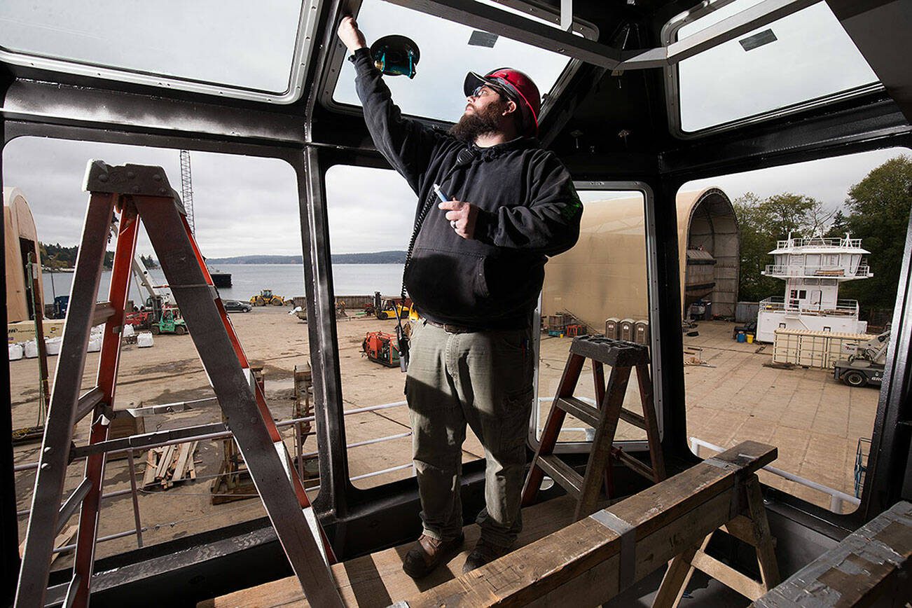 Shipfitter Wes Helseth installs windows into the pilothouse for a 100 foot tug at Nichols Brothers Boat Builders on Thursday, Oct. 25, 2018 in Freeland, Washington. Another pilothouse sits in the shipyard at right. (Andy Bronson / The Herald)