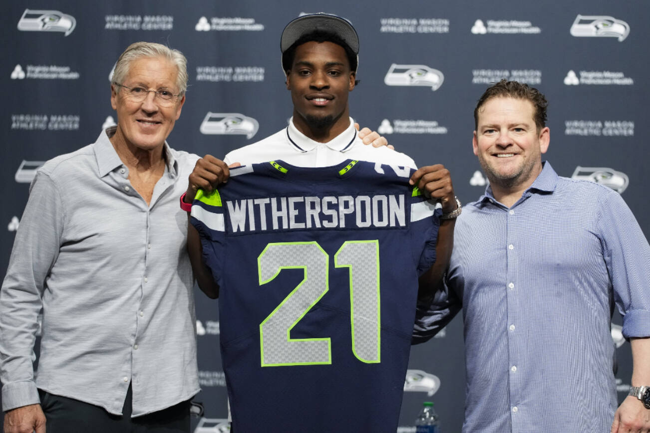 Seattle Seahawks first-round NFL football draft pick Devon Witherspoon, a cornerback from Illinois, holds up his jersey with head coach Pete Carroll, left, and general manager John Schneider, right, Friday, April 28, 2023, during a press conference at the team's headquarters in Renton, Wash. (AP Photo/Lindsey Wasson)