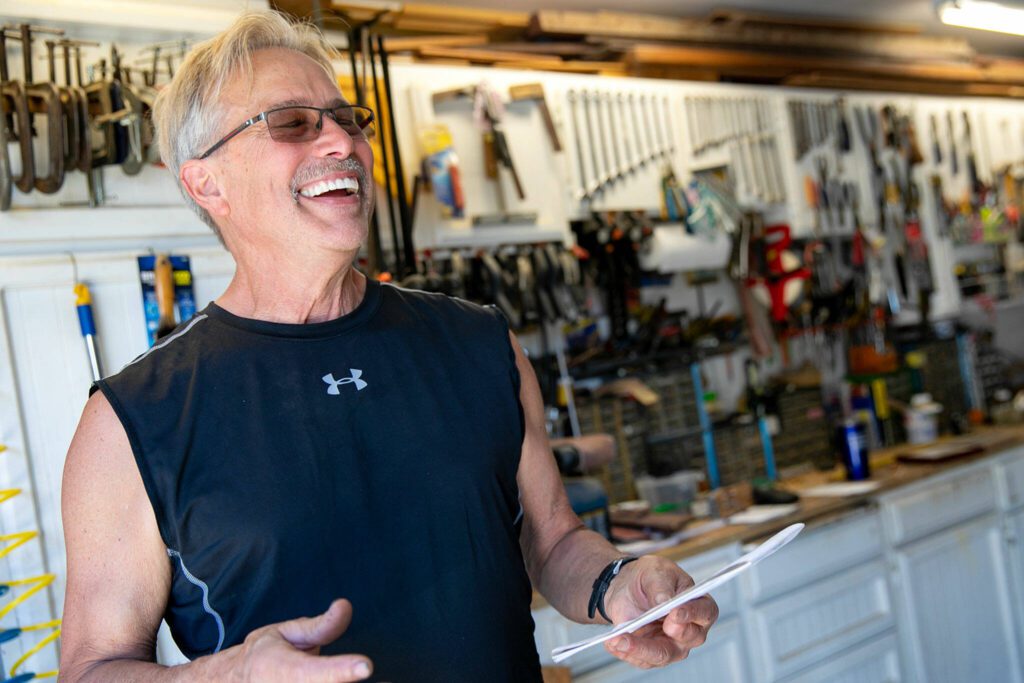 Gary Fontes laughs while reading over some hand-written notes in his garage workspace on Friday, May 12, 2023, at his home near Silver Lake in Everett, Washington. (Ryan Berry / The Herald)
