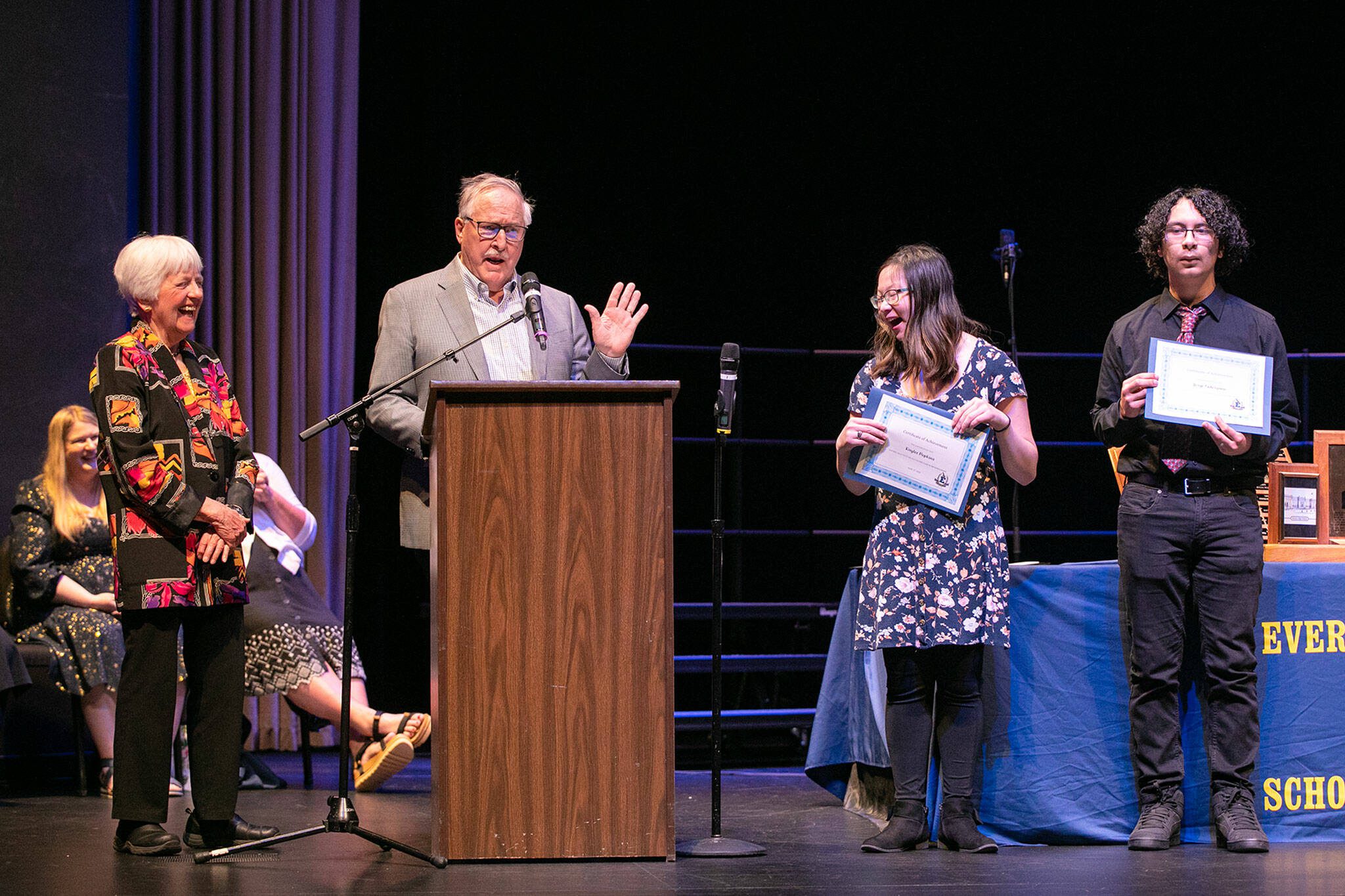 Peter Newland, speaking alongside fellow Everett High School Class of 1963 classmate June Remboldt Aprille, left, jokes with scholarship recipients Kaylee Popkins, right, and Jorge Solorzano, far right, during the school’s Scholarship Awards Night at the Everett Civic Auditorium. (Ryan Berry / The Herald)