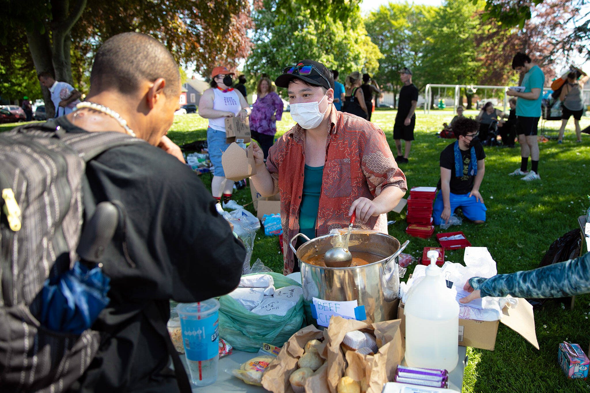 Volunteers help distribute food during a community gathering meant to provide resources in protest of Everett’s expanded “no sit, no lie” ordinance Sunday, May 14, 2023, at Clark Park in Everett, Washington. (Ryan Berry / The Herald)