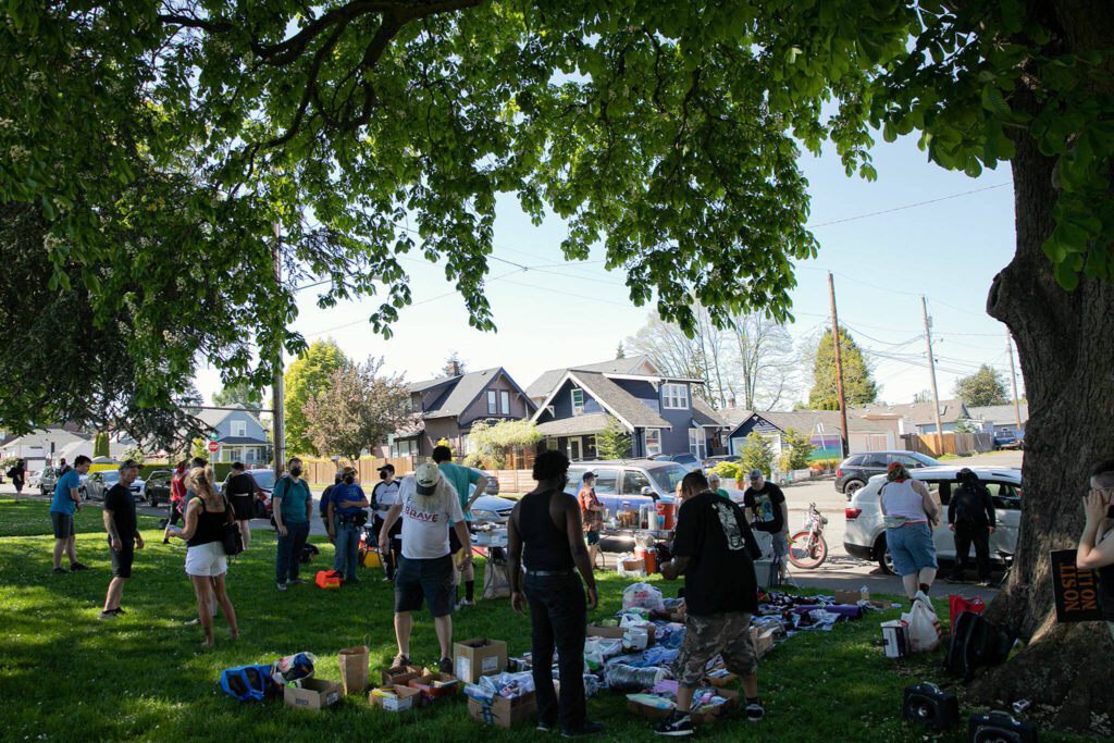 People gather in the shade during a community gathering to distribute food and resources in protest of Everett’s expanded “no sit, no lie” ordinance Sunday, May 14, 2023, at Clark Park in Everett, Washington. (Ryan Berry / The Herald)
