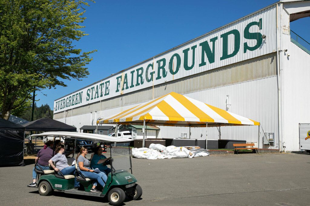 People zip around the fairgrounds on a golf cart as preparations for the state fair are underway on Monday, Aug. 22, 2022, at the Evergreen State Fairgrounds in Monroe, Washington. (Ryan Berry / The Herald) 
